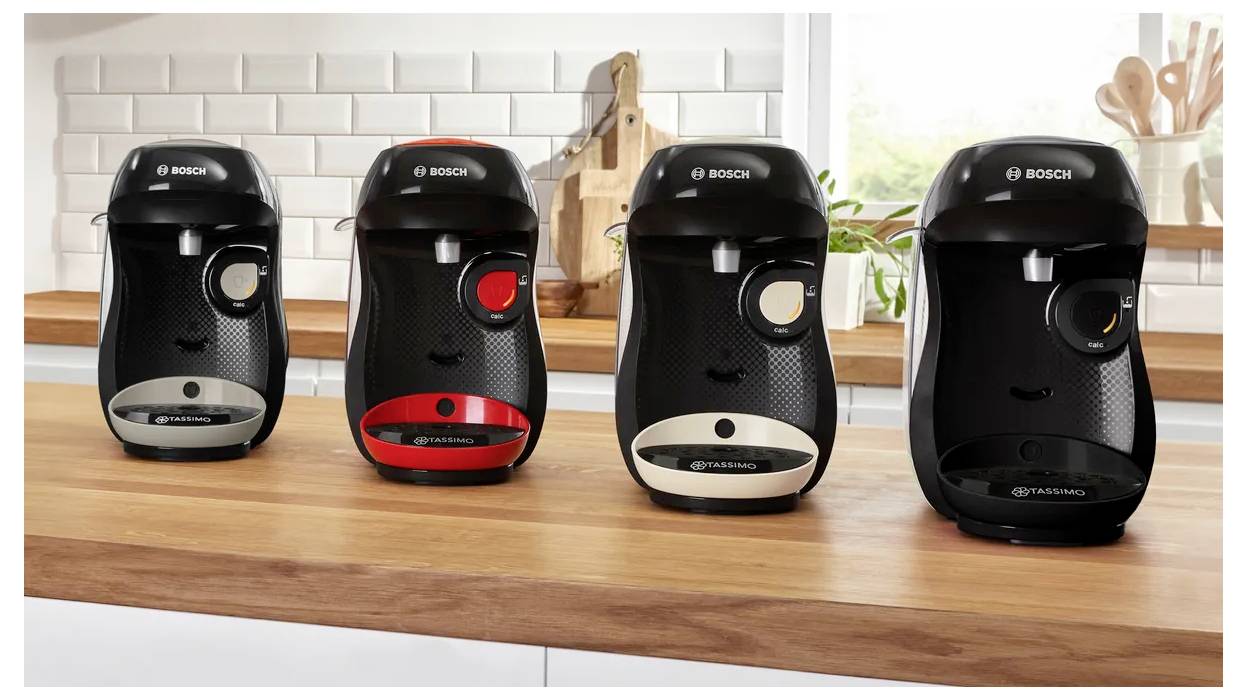 Vier zwarte Bosch koffiemachines zijn op een houten aanrecht geplaatst in een keukensetting met een wit betegelde achterwand.