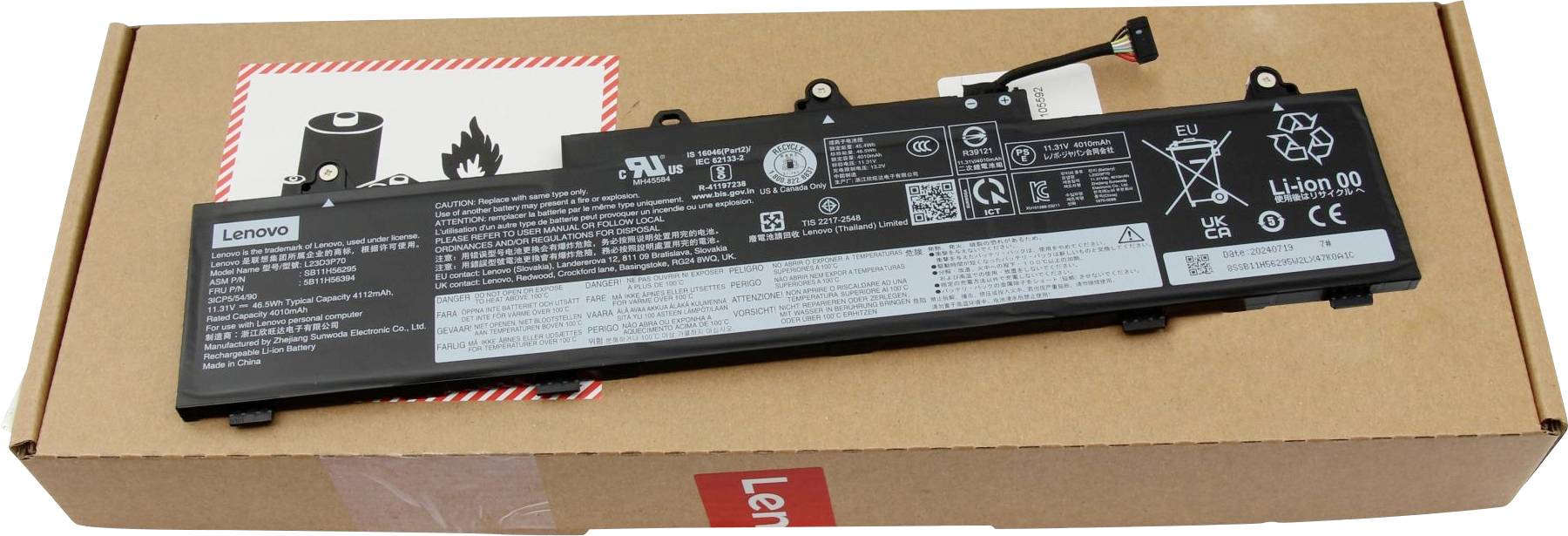 Een laptopbatterij rust op een kartonnen doos, voorzien van veiligheidssymbolen en fabrikantinformatie.