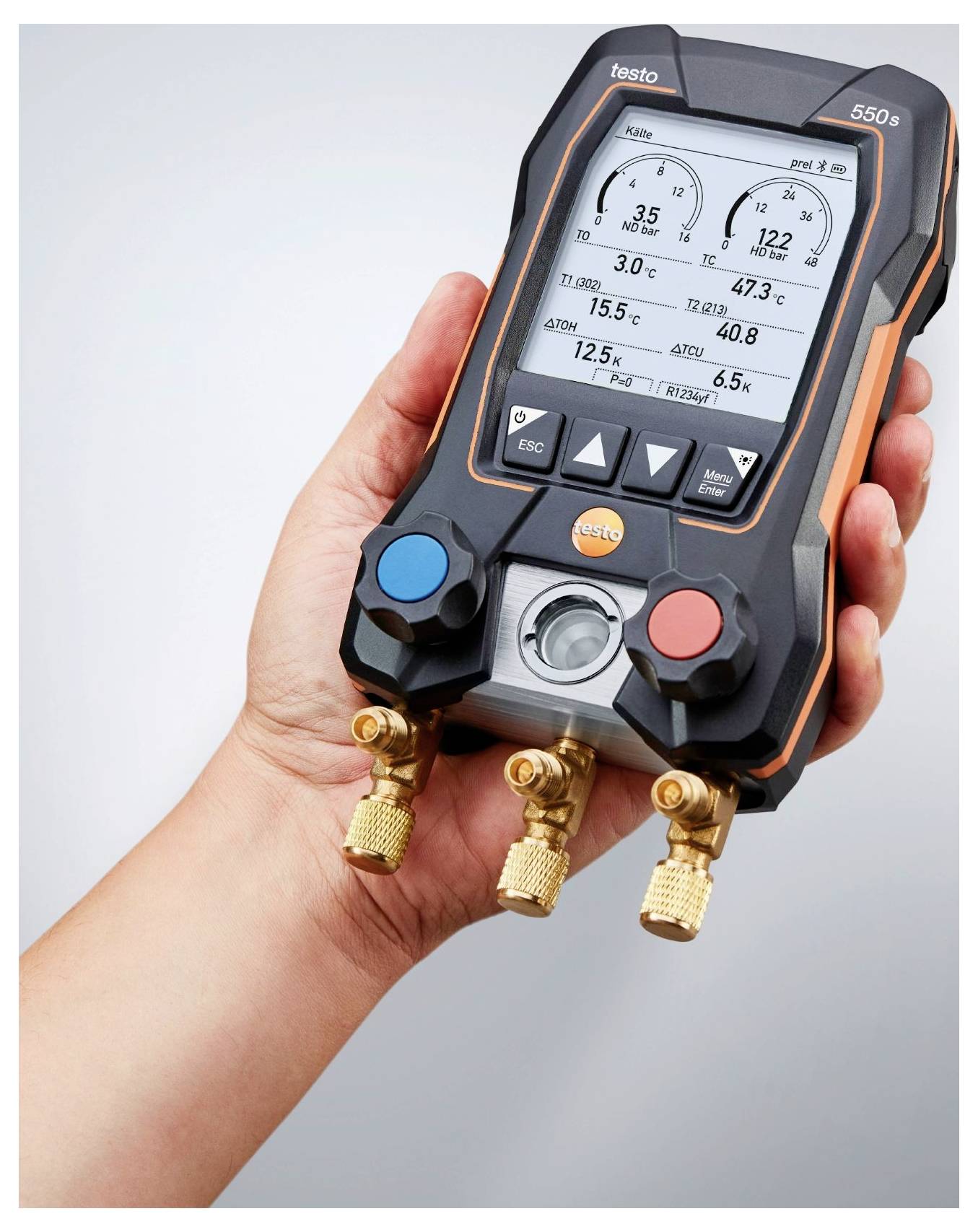 Een hand houdt een digitale HVAC-meter vast die druk- en temperatuurmetingen weergeeft, met drie messing aansluitingen onderaan.