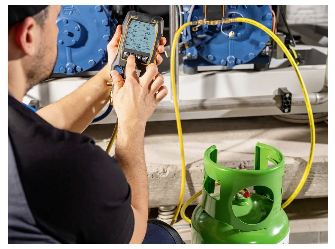 Een persoon gebruikt een digitaal apparaat om aflezingen te controleren, waarschijnlijk temperatuur of druk, met een groene gasfles nabij in een industriële omgeving.