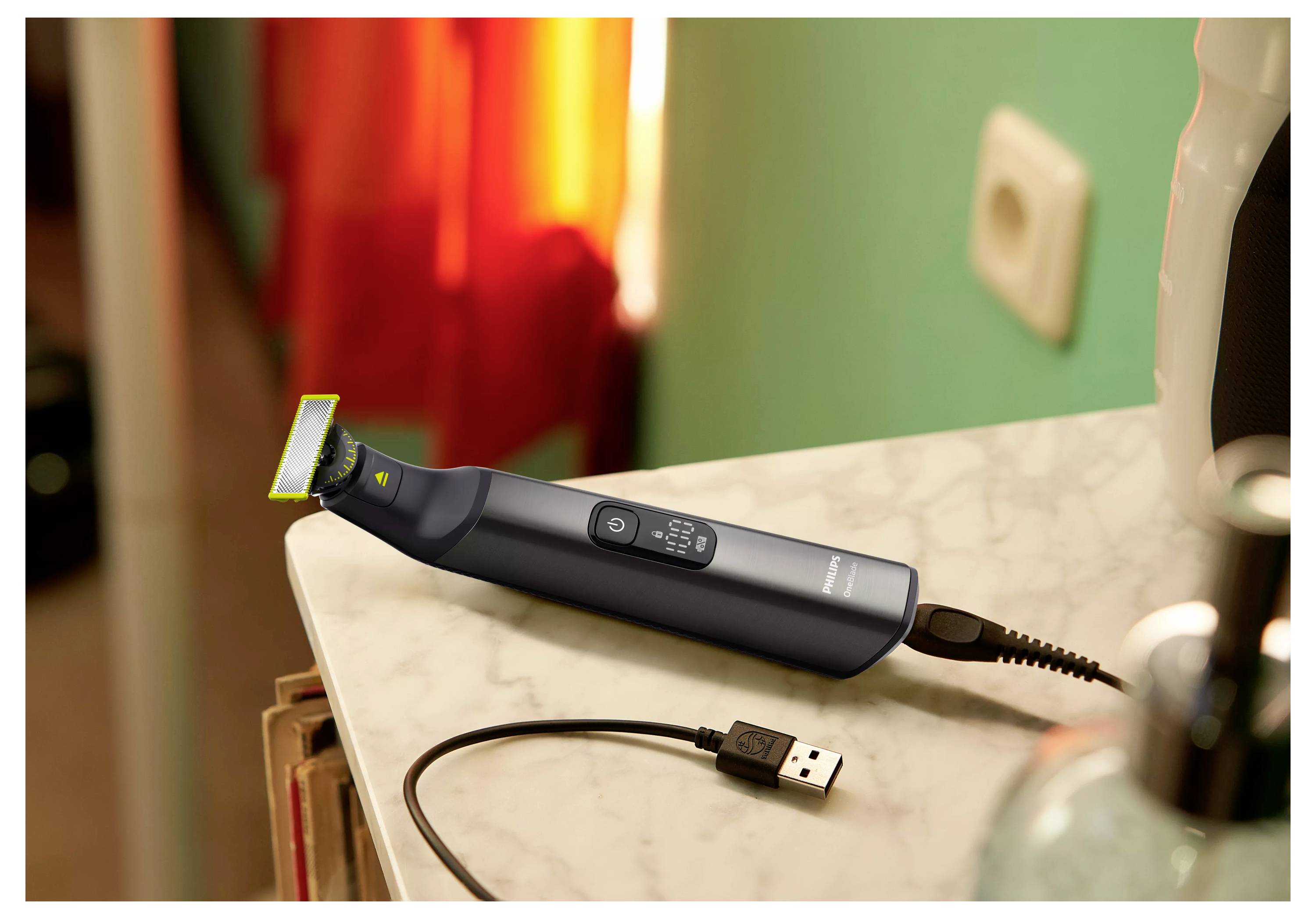 Een zwarte en limoengroene elektrische trimmer die op een marmeren aanrecht rust, verbonden met een USB-oplaadkabel, met een onscherpe kamers op de achtergrond.