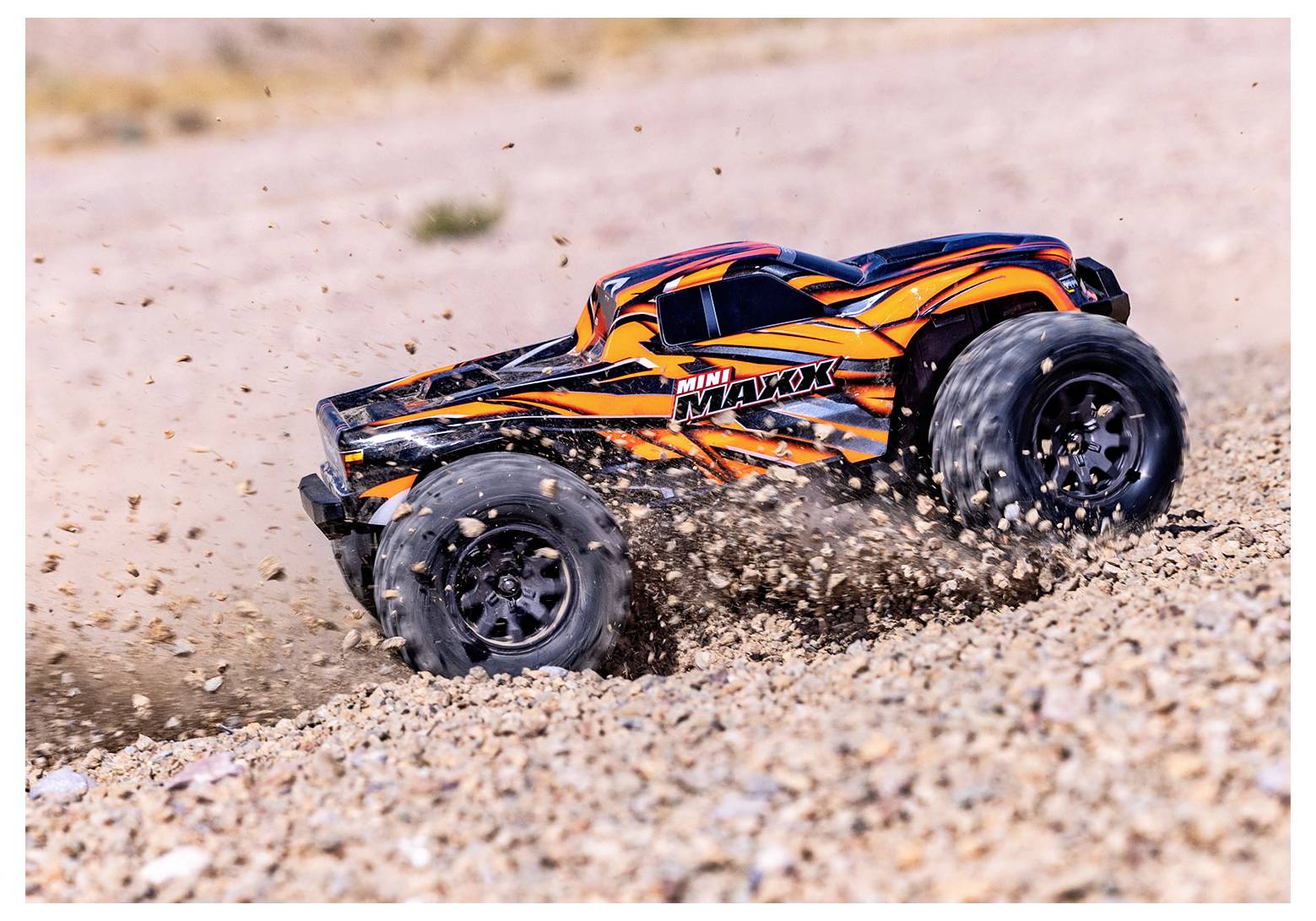 Een op afstand bestuurbare auto met een levendig oranje en zwart design raast over rotsachtig terrein, stof en grind opwerpend.