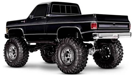 Een opgeheven vintage zwarte pickup truck met overgedimensioneerde banden, chromen velgen, en een Chevrolet-logo aan de achterkant, bekeken vanuit de achterste hoek.