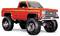 Een oranje klassieke pickup truck met grote, terreinbanden en een verhoogde ophanging, die zijn robuuste en gemodificeerde uitstraling benadrukt.