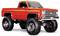 Een feloranje vintage pickup truck met buitenproportionele terreinbanden en een verhoogde ophanging, die een klassiek robuust ontwerp laat zien.