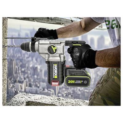 Een persoon gebruikt een Worx 20V accu-boor om een gat in een betonnen muur te maken, draagt handschoenen en staat op een bouwplaats op grote hoogte.