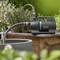 Een zwarte Gardena waterpomp aangesloten op een tuinslang, geplaatst naast een rond stenen waterbekken, omringd door groene planten.