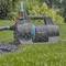 Een zwarte en blauwe elektrische tuinwaterpomp spuit water over een groen grasveld, met bomen vaag op de achtergrond.