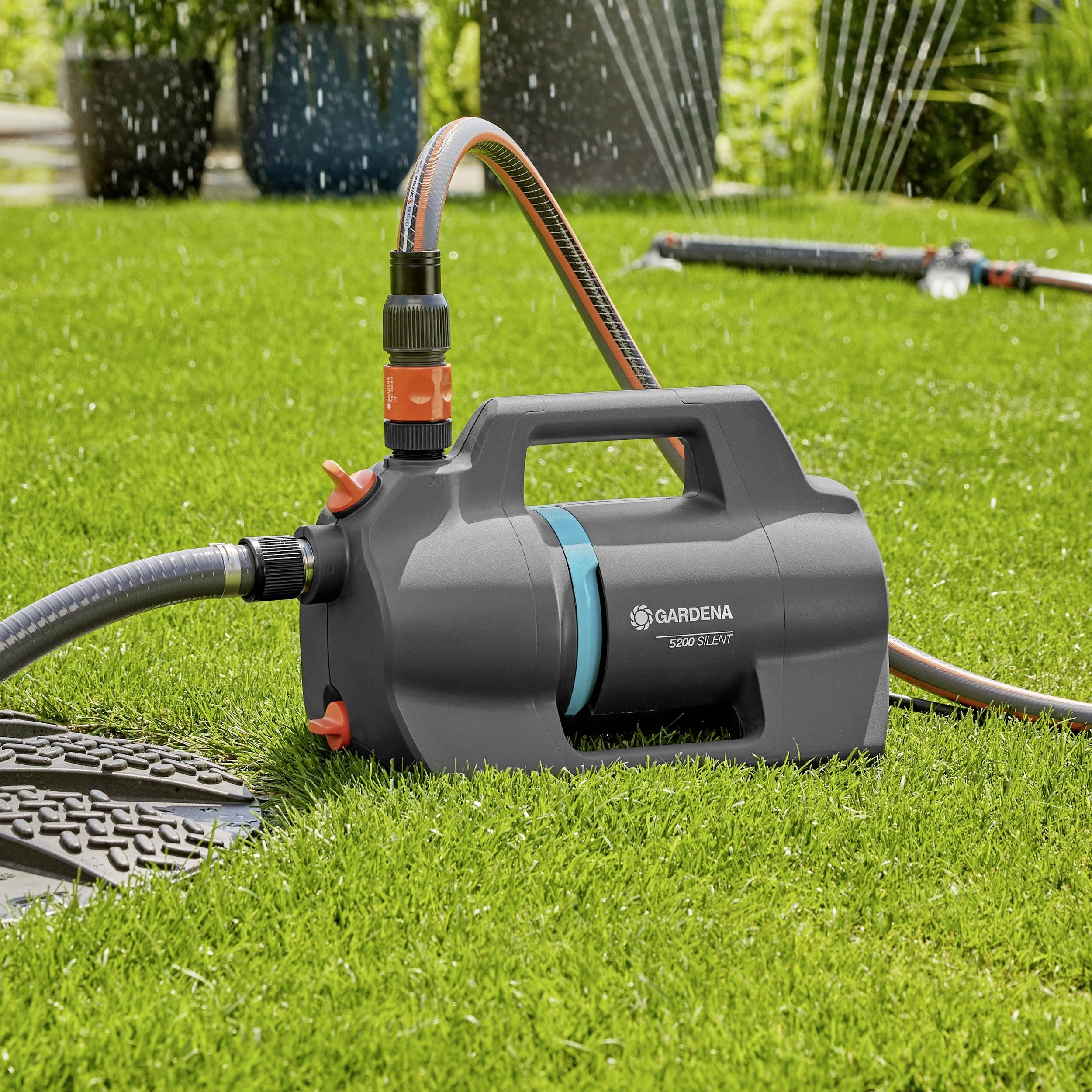 Een tuinslanghouder met een feloranje handvat op een groen gazon, met watersproeiers op de achtergrond.
