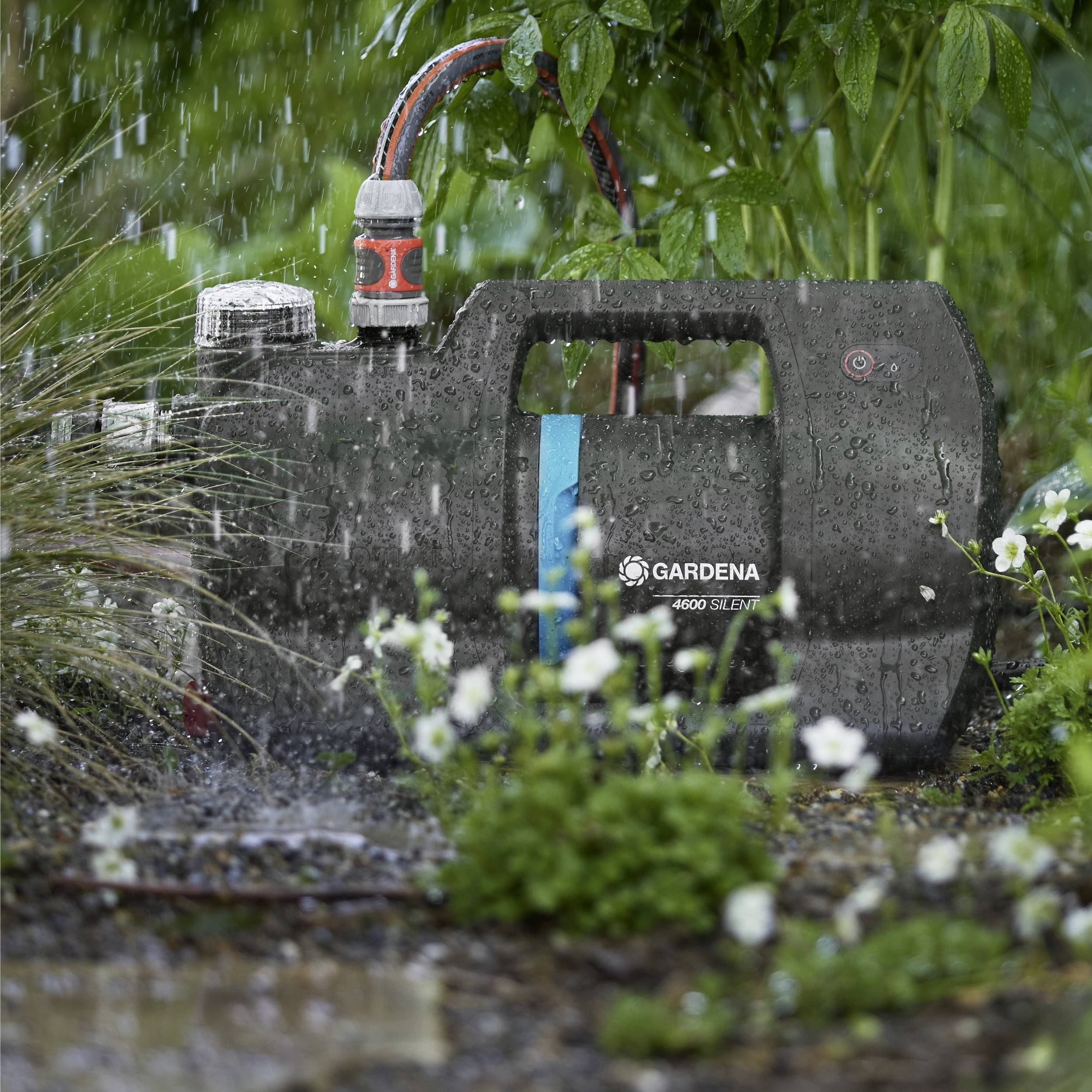 Draagbare waterpomp in een regenachtige tuinomgeving, omringd door planten, die de waterstroom efficiënt omleidt door middel van een uitloop en aangesloten slang.