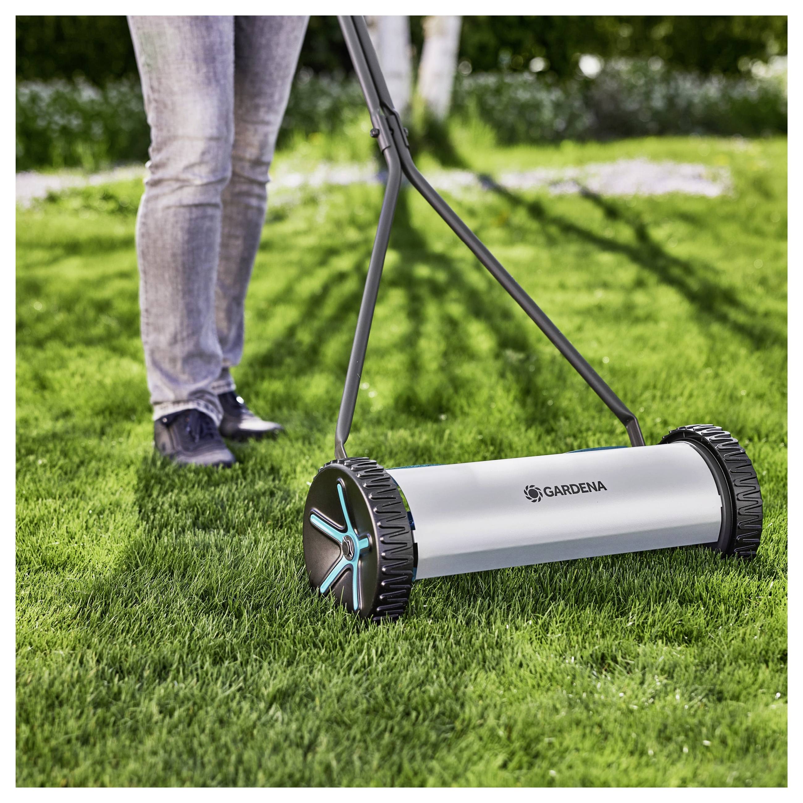 Een persoon die op een zonnige dag een gazon maait met een handmatige spoelmaaier, met nadruk op het ontwerp van de maaier en het weelderige groene gras.