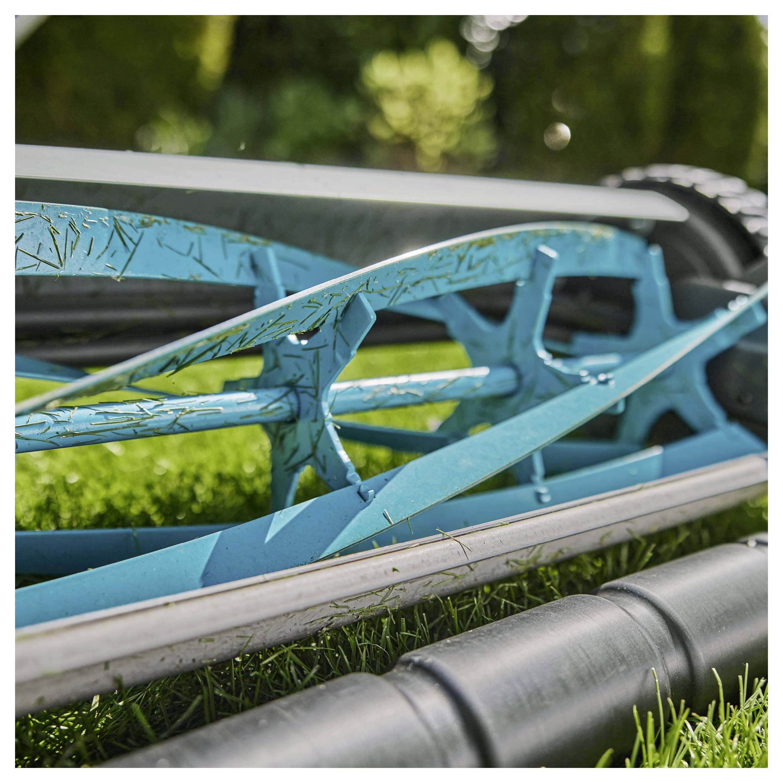 Een blauwe handmatige grasmaaier met scherpe messen rust op een netjes gemaaid grasperk, horizontaal in close-up weergegeven.