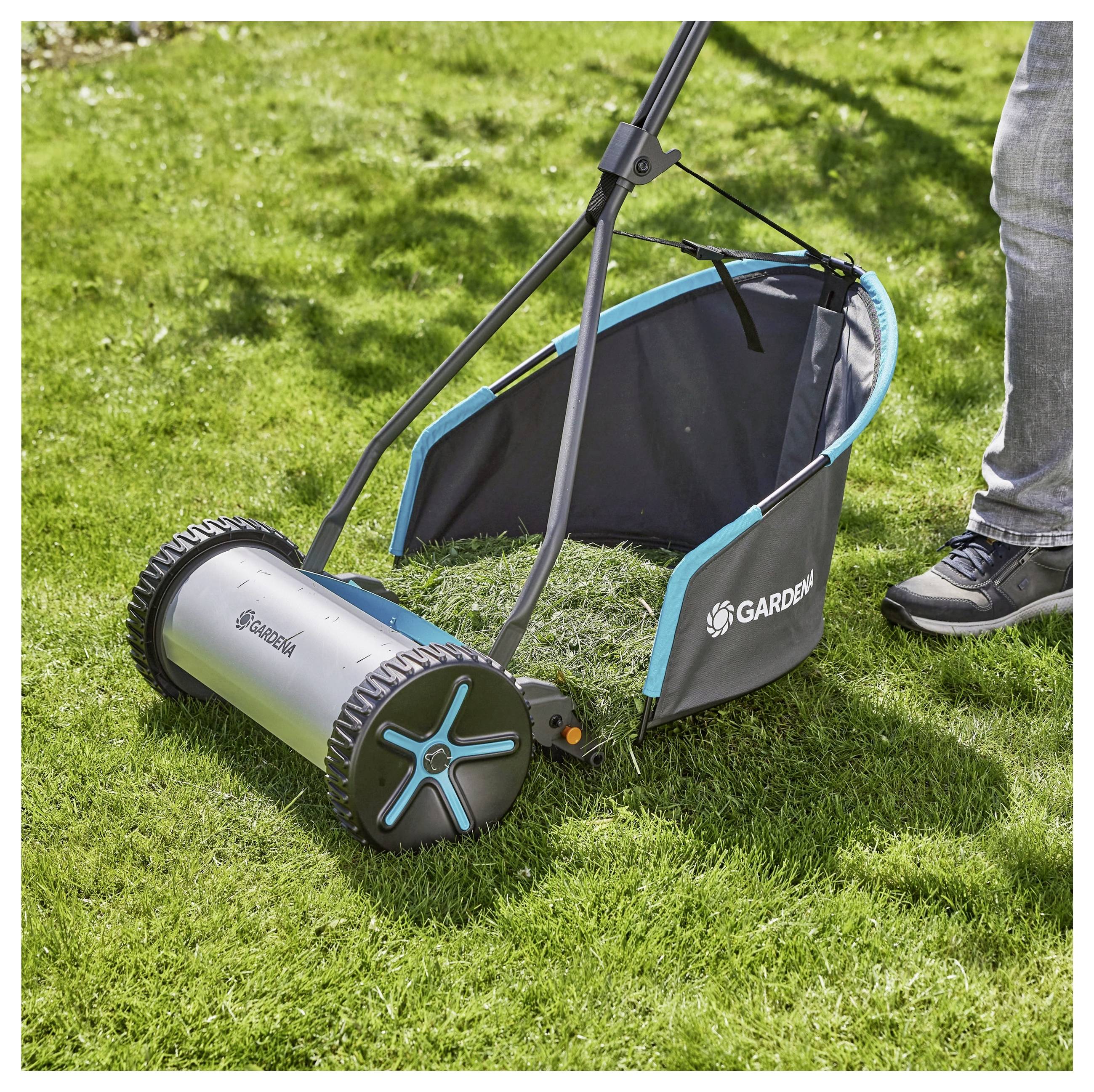 Een handmatige grasmaaier met een opvangmand; een persoon duwt deze over een groen gazon.