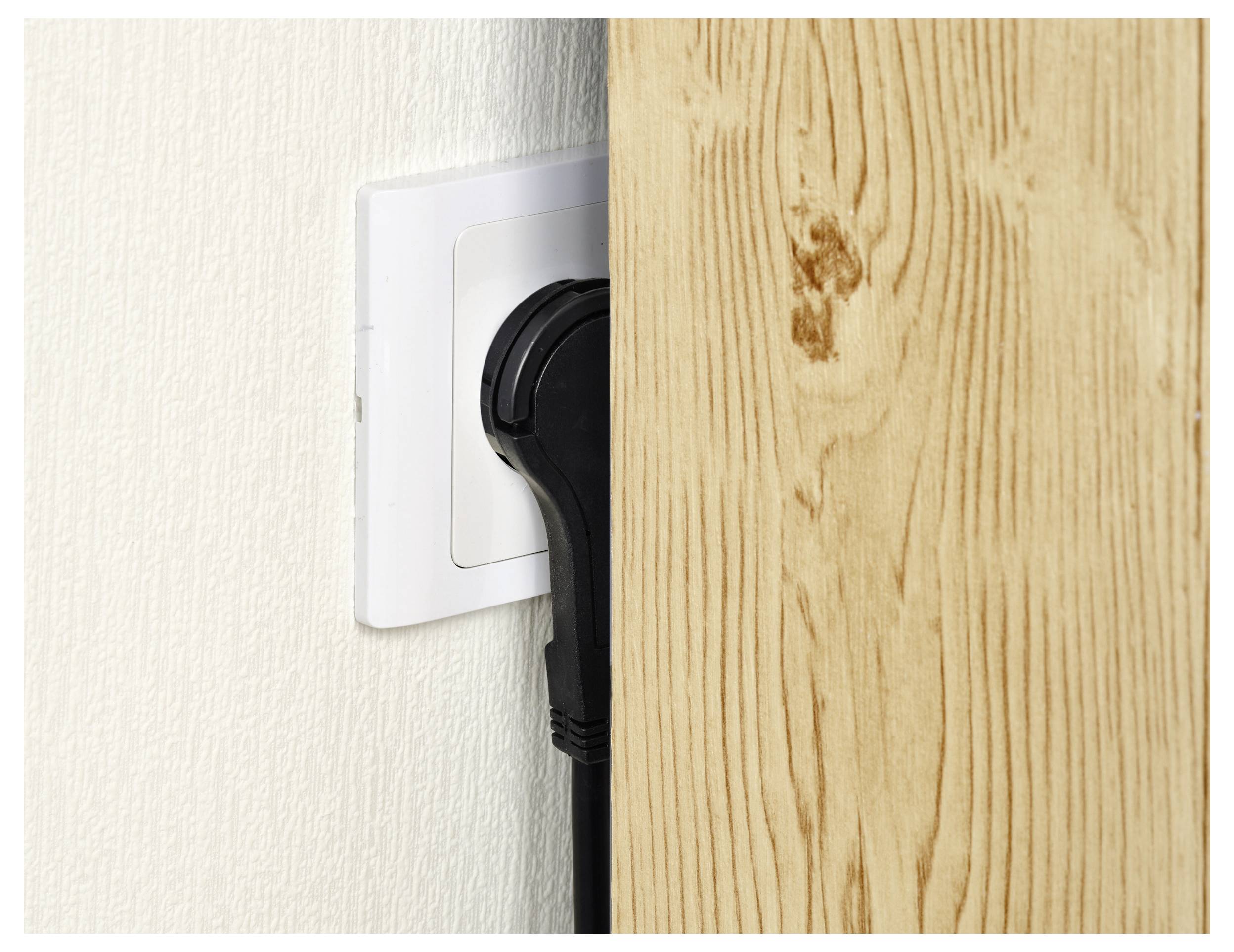 Een zwarte stekker wordt in een wit stopcontact gestoken met een houten paneel dicht ernaast, wat beperkte ruimte voor de stekker toont.