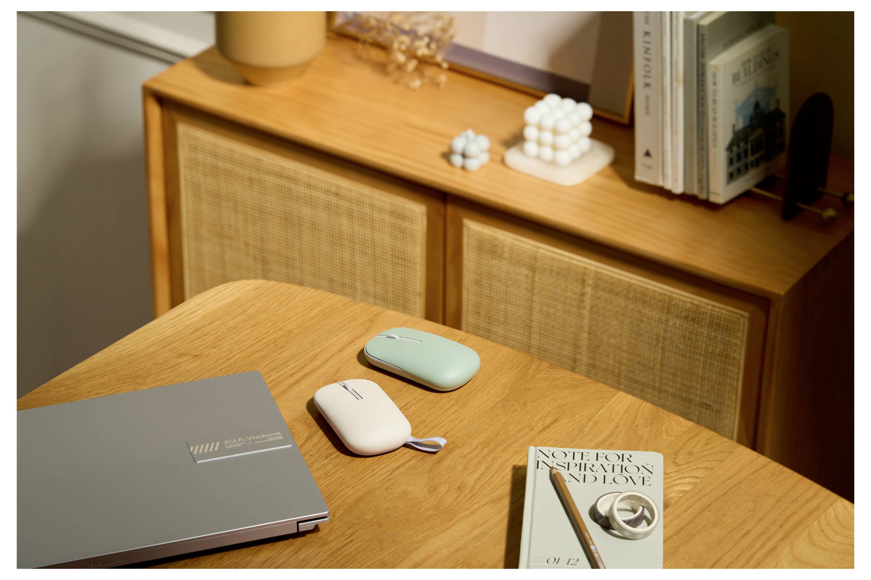 'Een houten bureau met twee draagbare elektronische apparaten, een boek met de titel 'Notebook Inspiraties en Liefde', en een gesloten laptop.'
