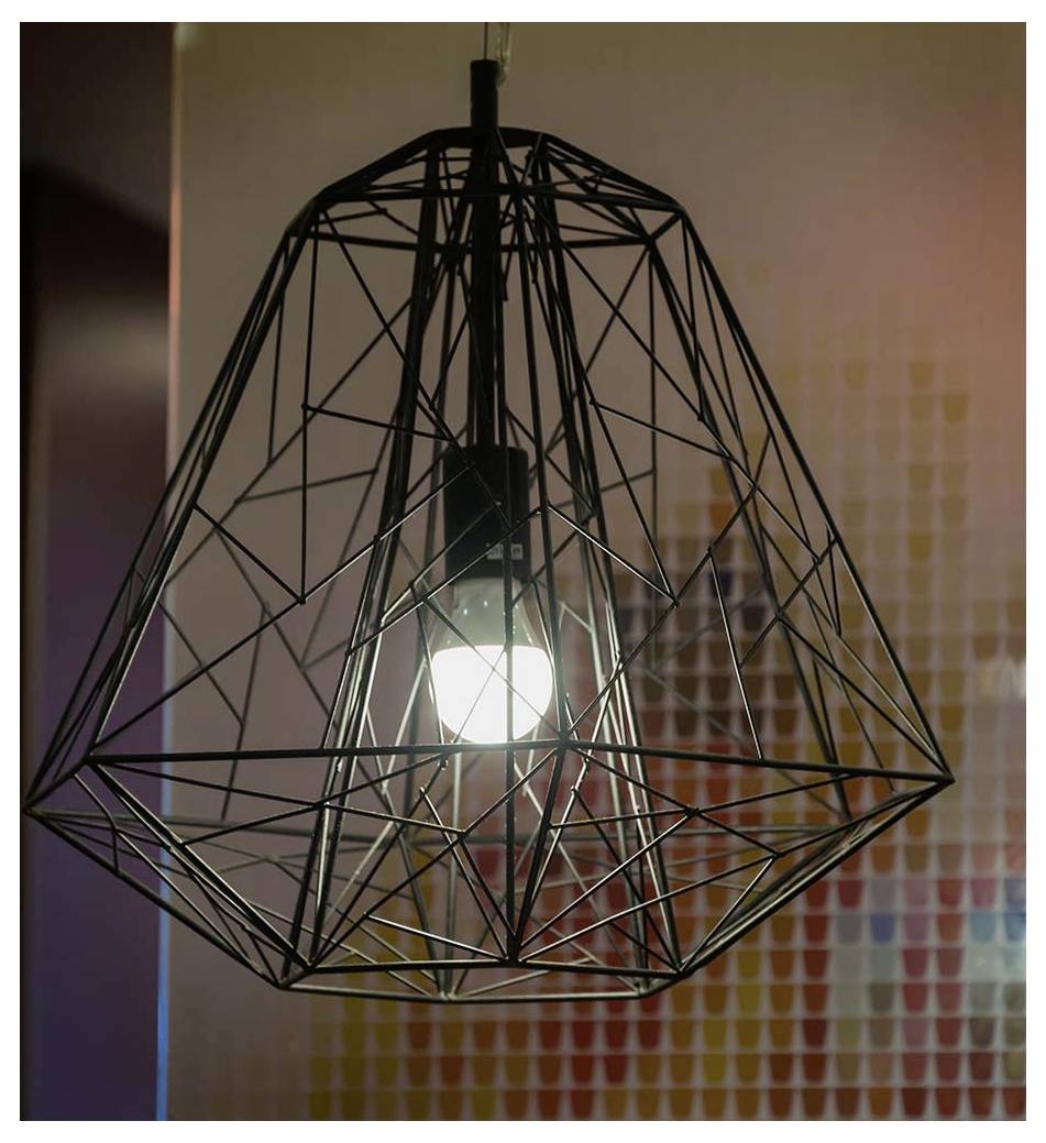 Een geometrisch draadframe lampenkap omringt een brandende lamp, die zacht licht verspreidt. De achtergrond is een wazig mozaïek van zachte kleuren.