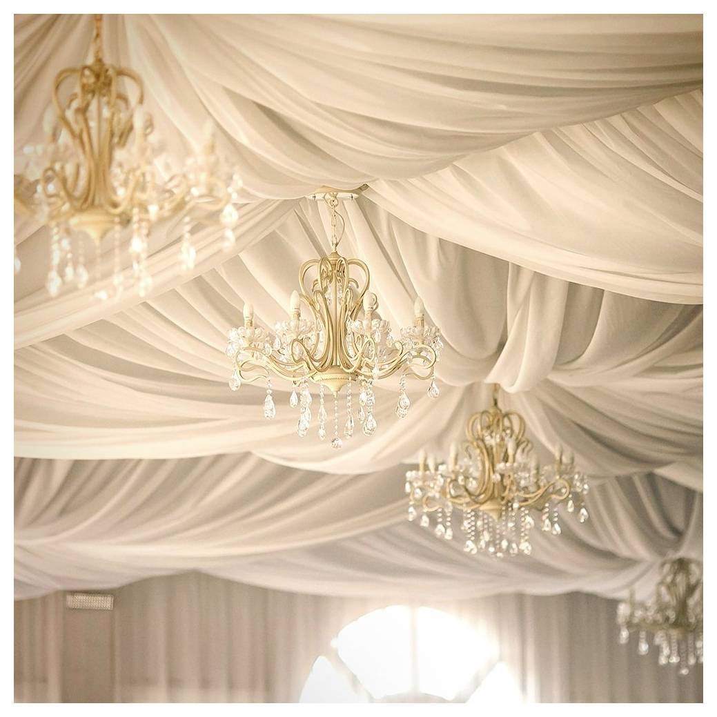 Elegant plafond behangen met wit stof en versierd met sierlijke, gouden kroonluchters voorzien van neerdalende kristallen accenten.