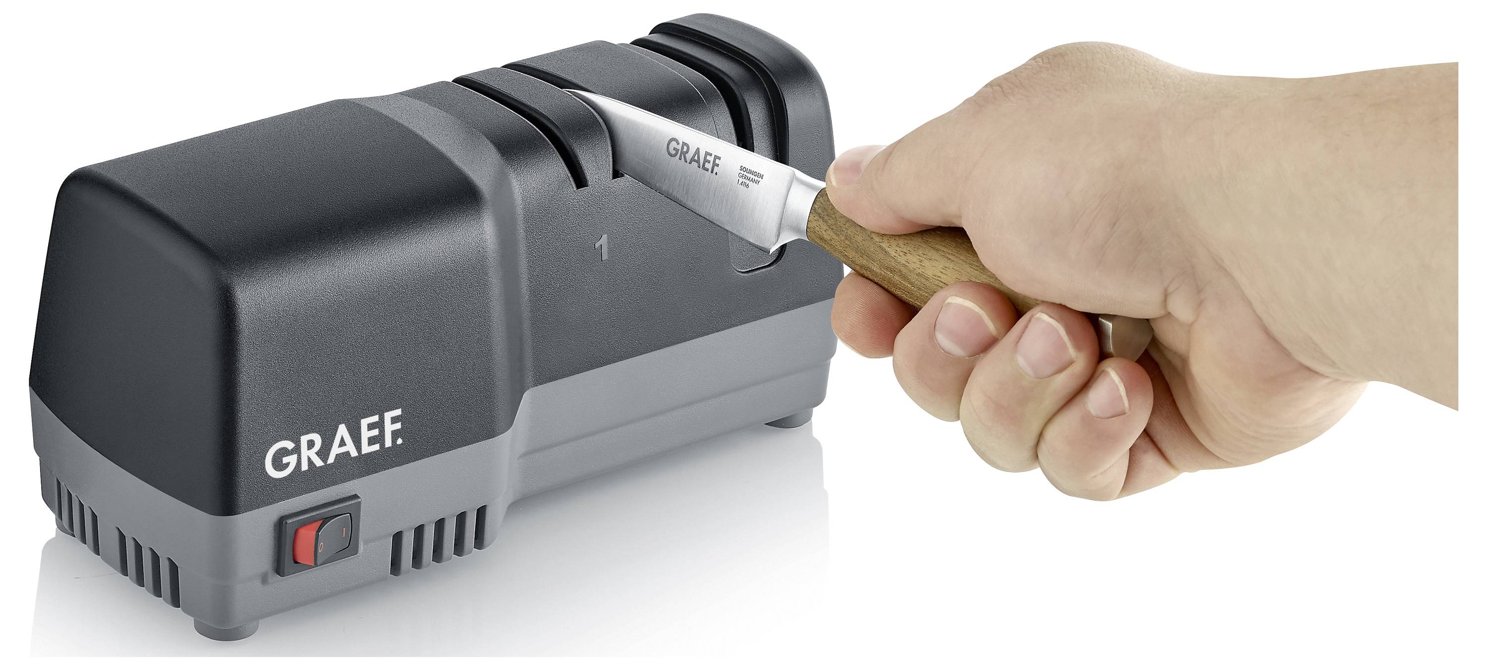 Een hand scherpt een mes met een elektrische messenslijper, waarbij het merk 'Graef' zichtbaar is op het apparaat.