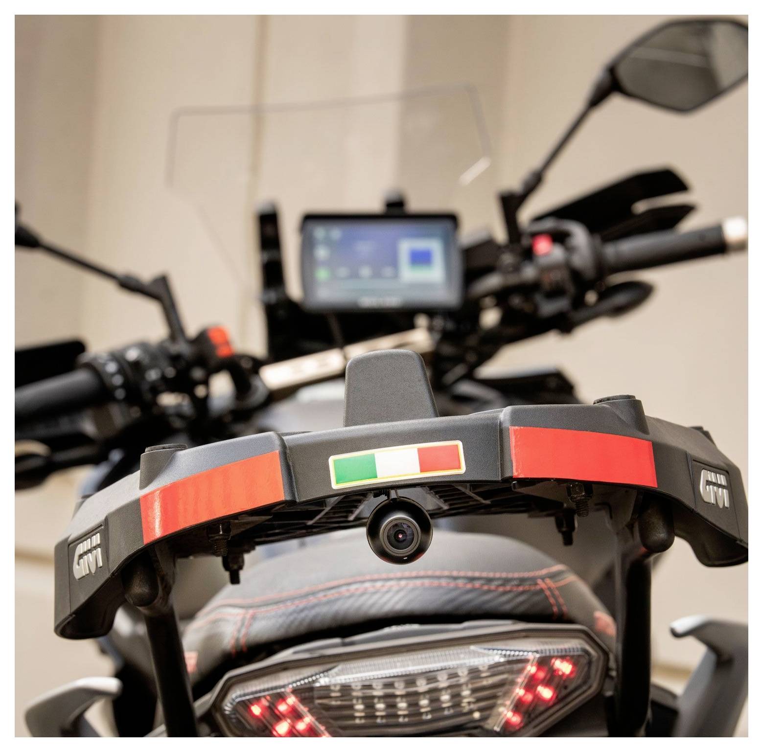 Achteraanzicht van een motorfiets met een Italiaanse vlag sticker op een topkoffer bevestiging, met een digitaal schermdisplay en een kentekenplaathouder.