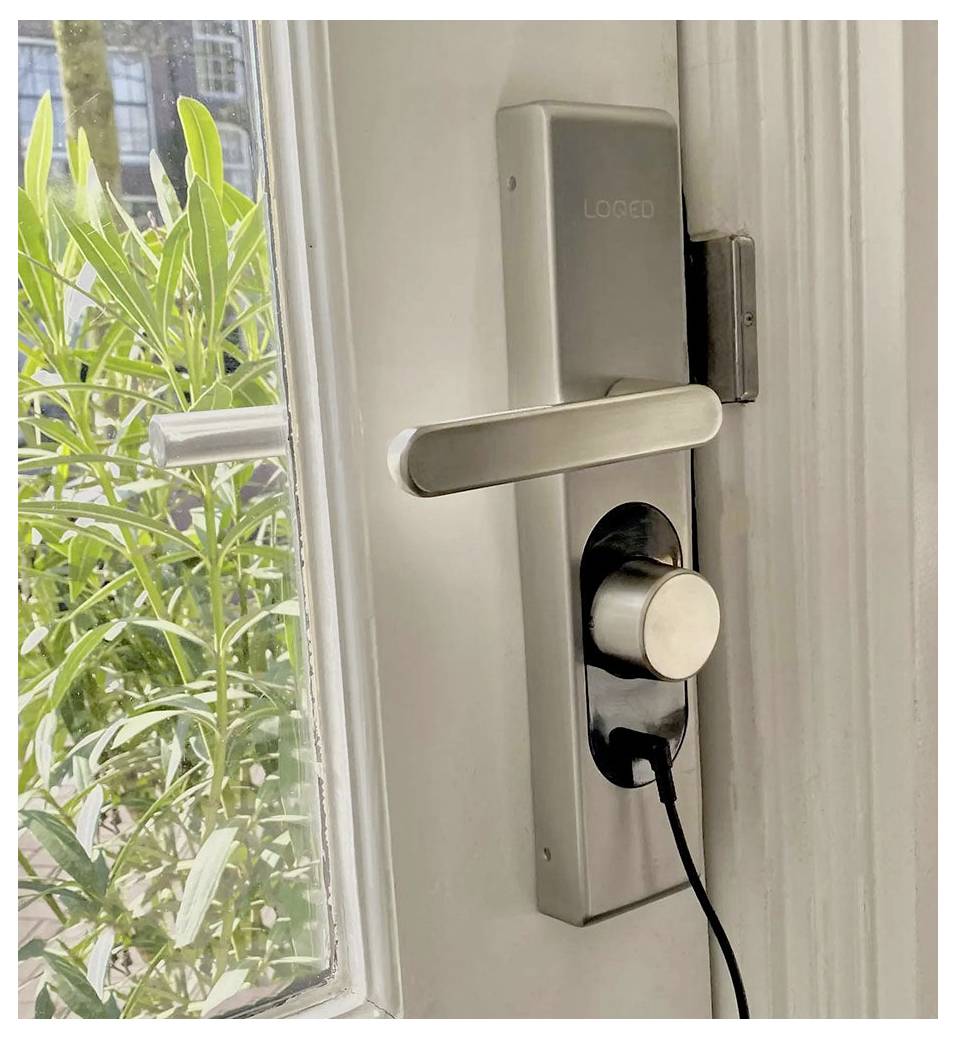 Een moderne zilverkleurige deurklink met een digitaal slot is geïnstalleerd op een witte deur, half open, waarbij buiten groene vegetatie zichtbaar is.