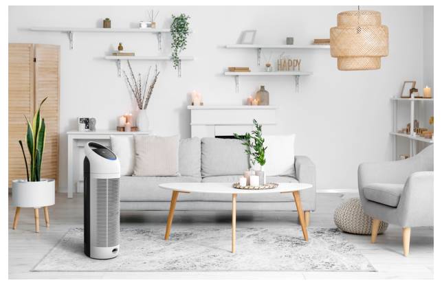 Een gezellige woonkamer met een grijze bank, een witte salontafel en potplanten. Een moderne luchtreiniger is prominent in de voorgrond geplaatst.
