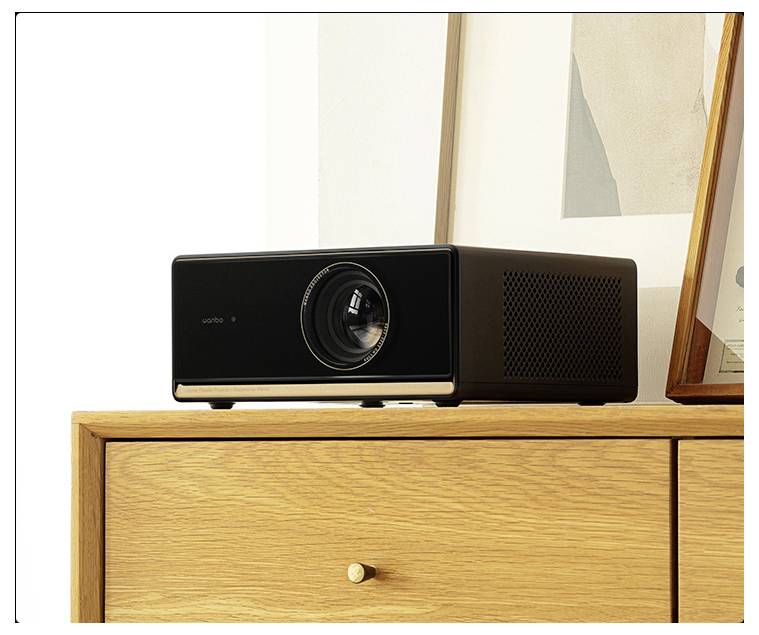 Een zwarte projector staat op een licht houten kast tegen een witte muur, omgeven door moderne kunst- en decoratieve elementen.