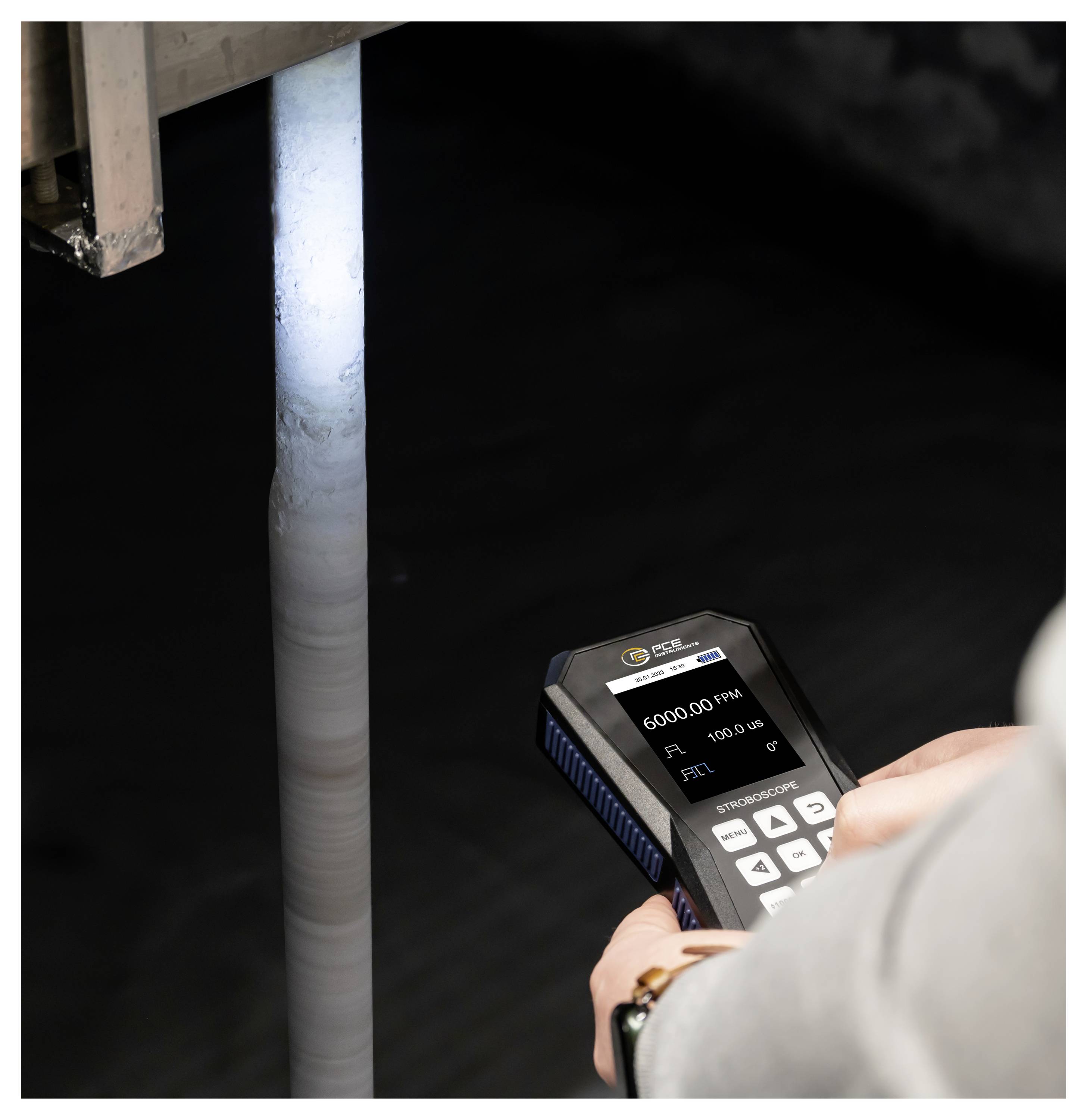 Een persoon gebruikt een handheld meter om een verticale pijp of kolom in een donkere industriële omgeving te meten, met het display dat 6000.00 RPM aangeeft.