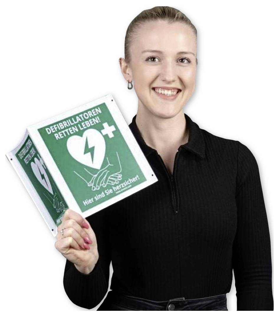 Een persoon glimlacht terwijl hij een groen bord vasthoudt met een wit hart- en kruissymbool. Het bord leest 'Defibrillatoren retten Leben!'.