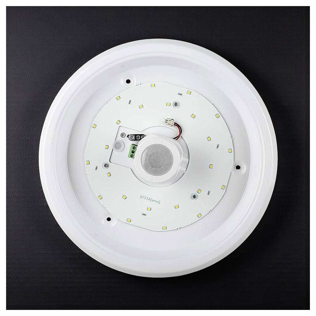 Een ronde LED-plafondlamp met een bewegingssensor in het midden, gemonteerd op een donker oppervlak. De sensor heeft zichtbare bedrading.