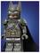 Een LEGO-figuur die lijkt op een superheld met een vleermuis-achtig masker en cape, in een grijs pak met een gereedschapsriem, staande tegen een blauwe achtergrond.