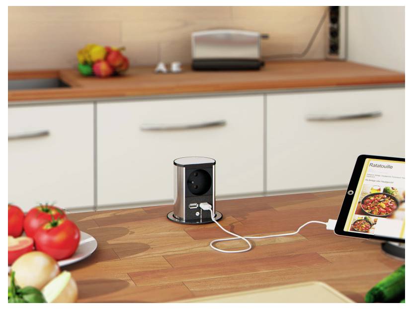 Een aanrecht in de keuken met fruit en een tablet waarop een 'Ratatouille'-recept wordt weergegeven. Een pop-up stopcontact laadt een apparaat op via USB.
