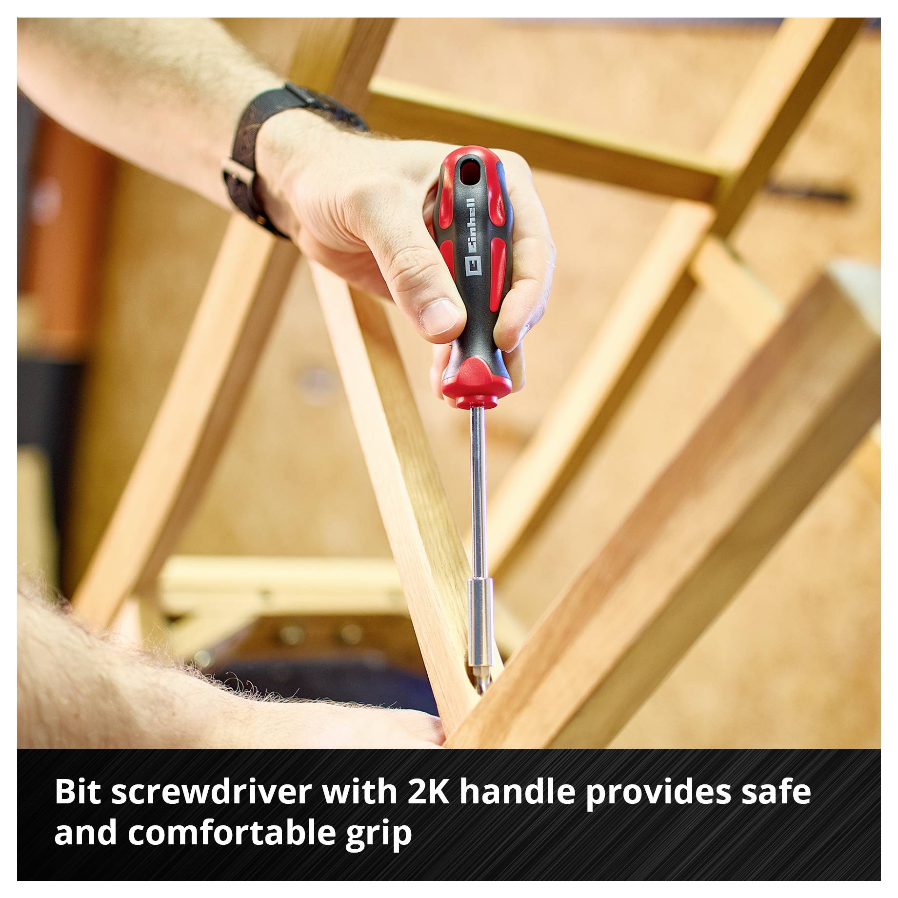 Een bitschroevendraaier met 2K-greep wordt gebruikt om een schroef in hout in te draaien. Tekst: 'Bitschroevendraaier met 2K-greep ligt veilig en comfortabel in de hand'.