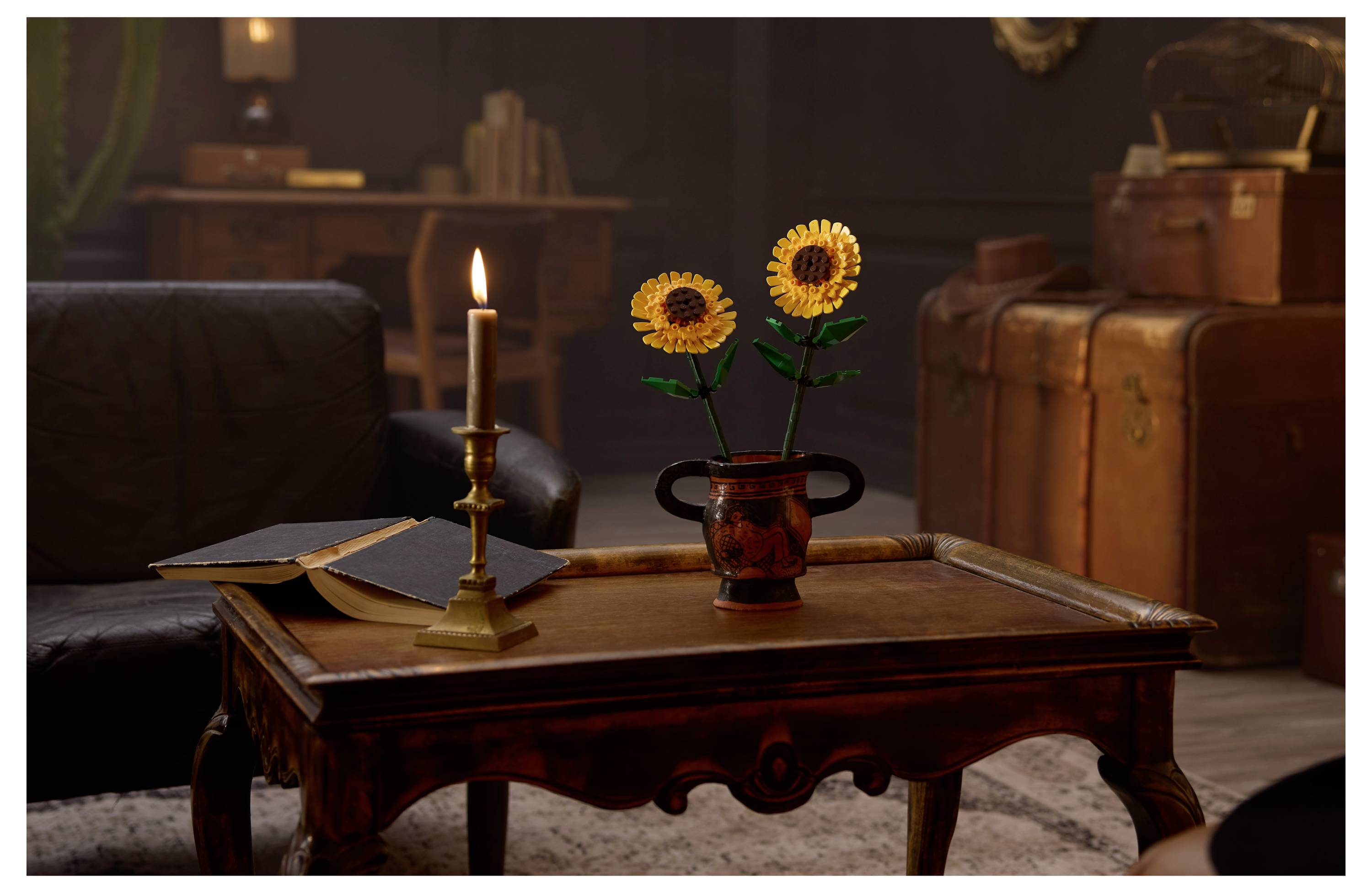 Een zwak verlichte kamer met een houten tafel, een kaars, een open boek en een vaas met zonnebloemen. Stapels bagage en boeken zijn zichtbaar op de achtergrond.