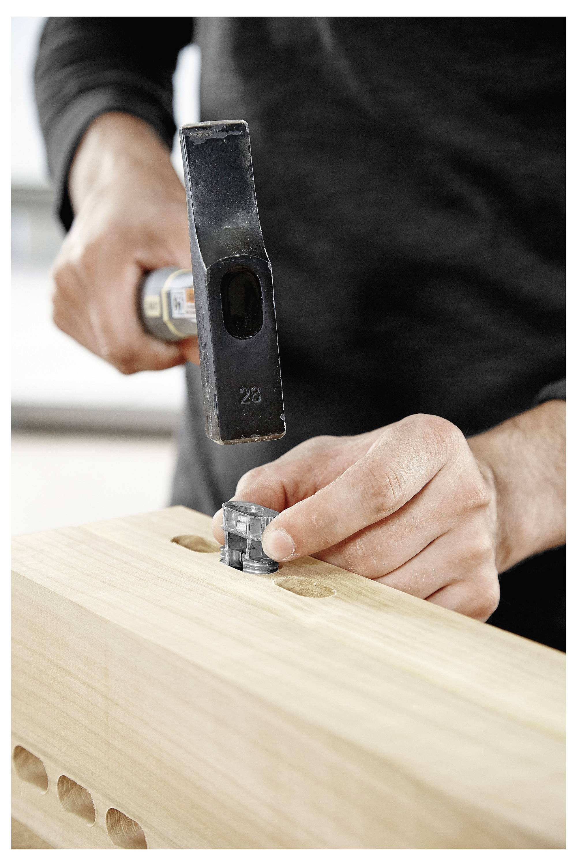 Een persoon gebruikt een hamer om een houten deuvel in een werkbankgat in te slaan, wat het houtbewerkingsmontage in uitvoering laat zien.