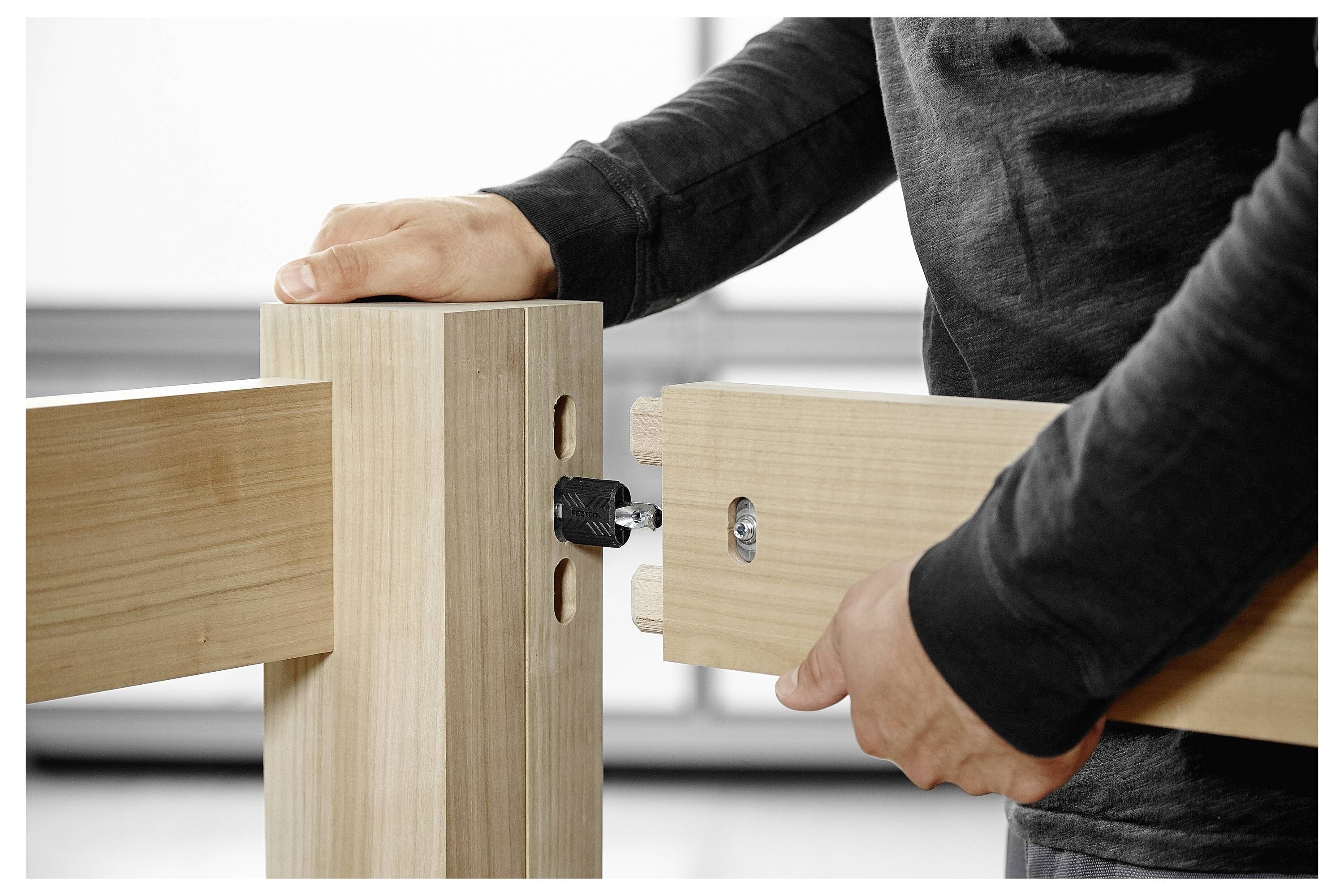 Een persoon in een zwart shirt assembleert een houten tafel, waarbij twee houten onderdelen met een bout worden verbonden om een stevig verbindingspunt te creëren.