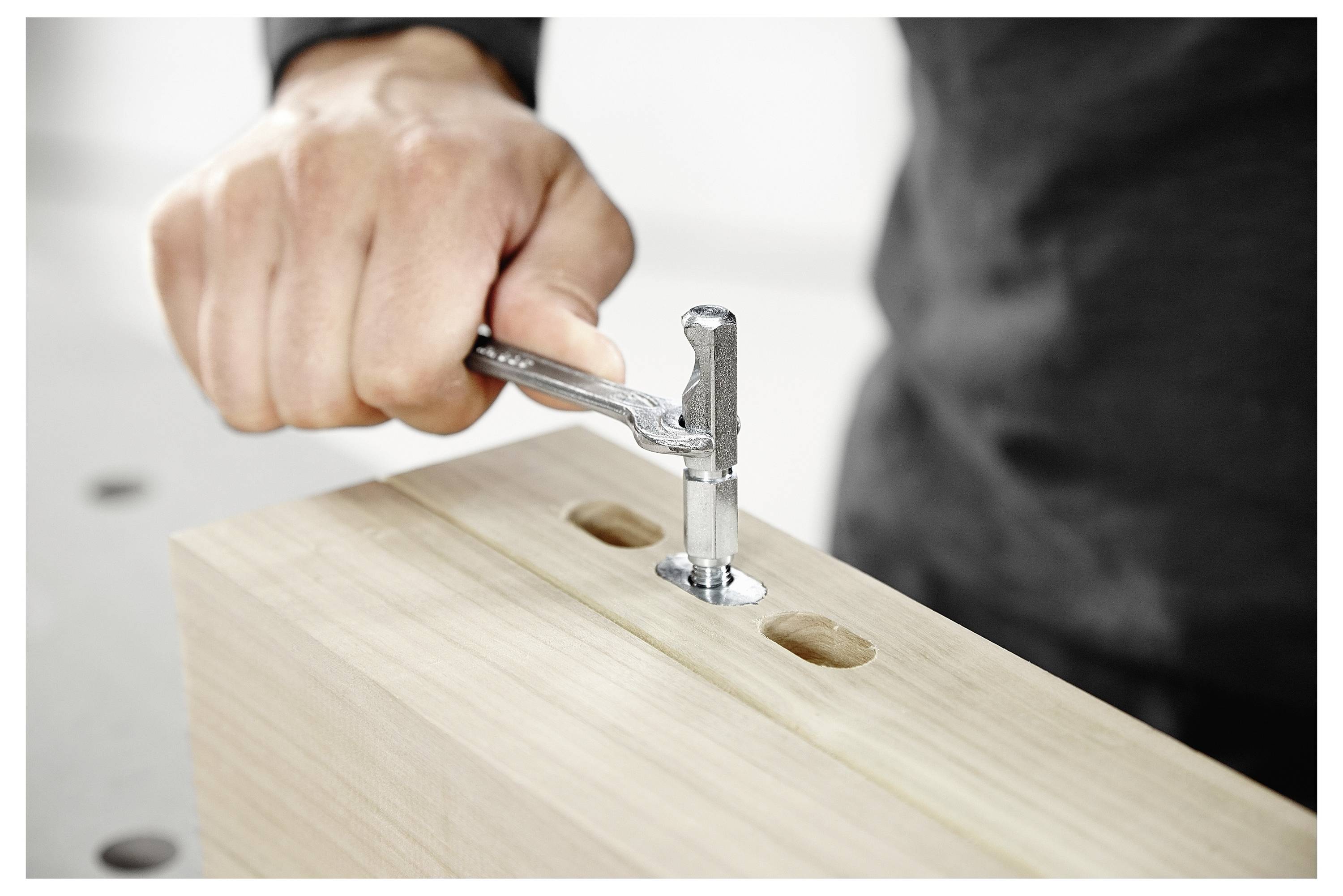 Een persoon die een opvouwbare werkbank met verstelbare hoogte en groene wielremmen samenstelt op een licht gekleurde vloer, in de buurt van grote ramen.