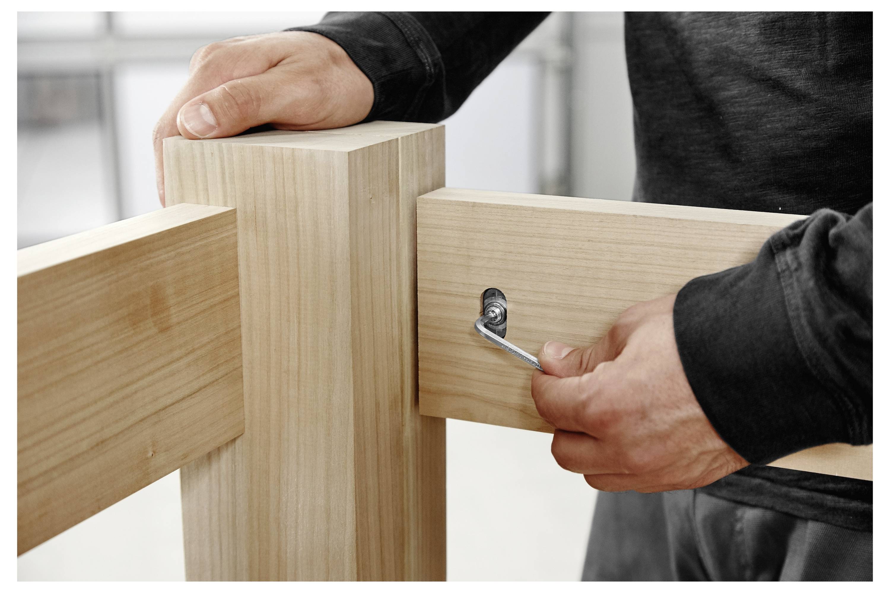 Persoon die houten meubels in elkaar zet, een zeskantige sleutel gebruikt om een bout aan te draaien, twee houten panelen verbindt.