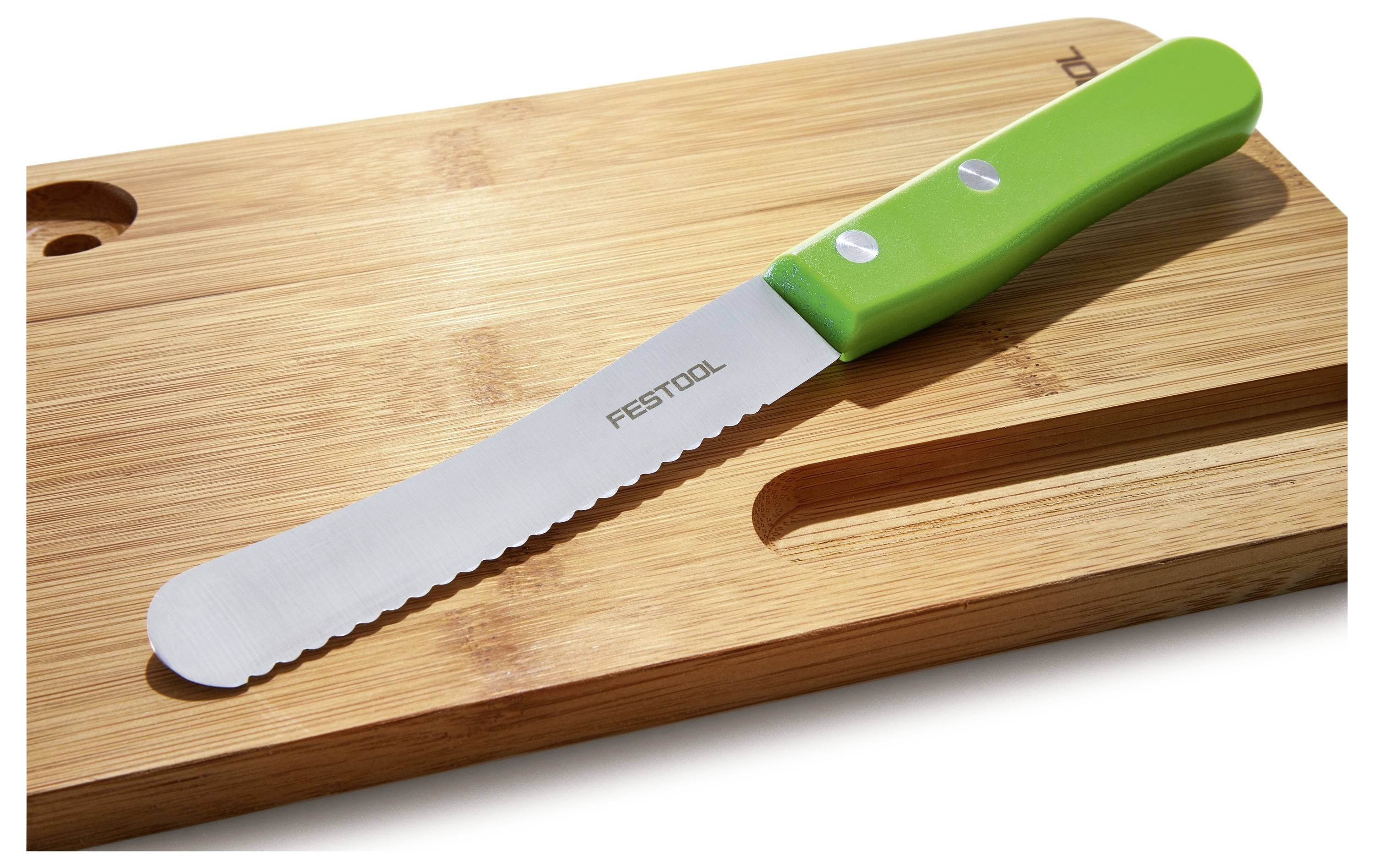 Een gekartelde mes met een groen handvat rust op een houten snijplank, wat doet vermoeden dat het gereedschap is voor het snijden of hakken van voedsel.