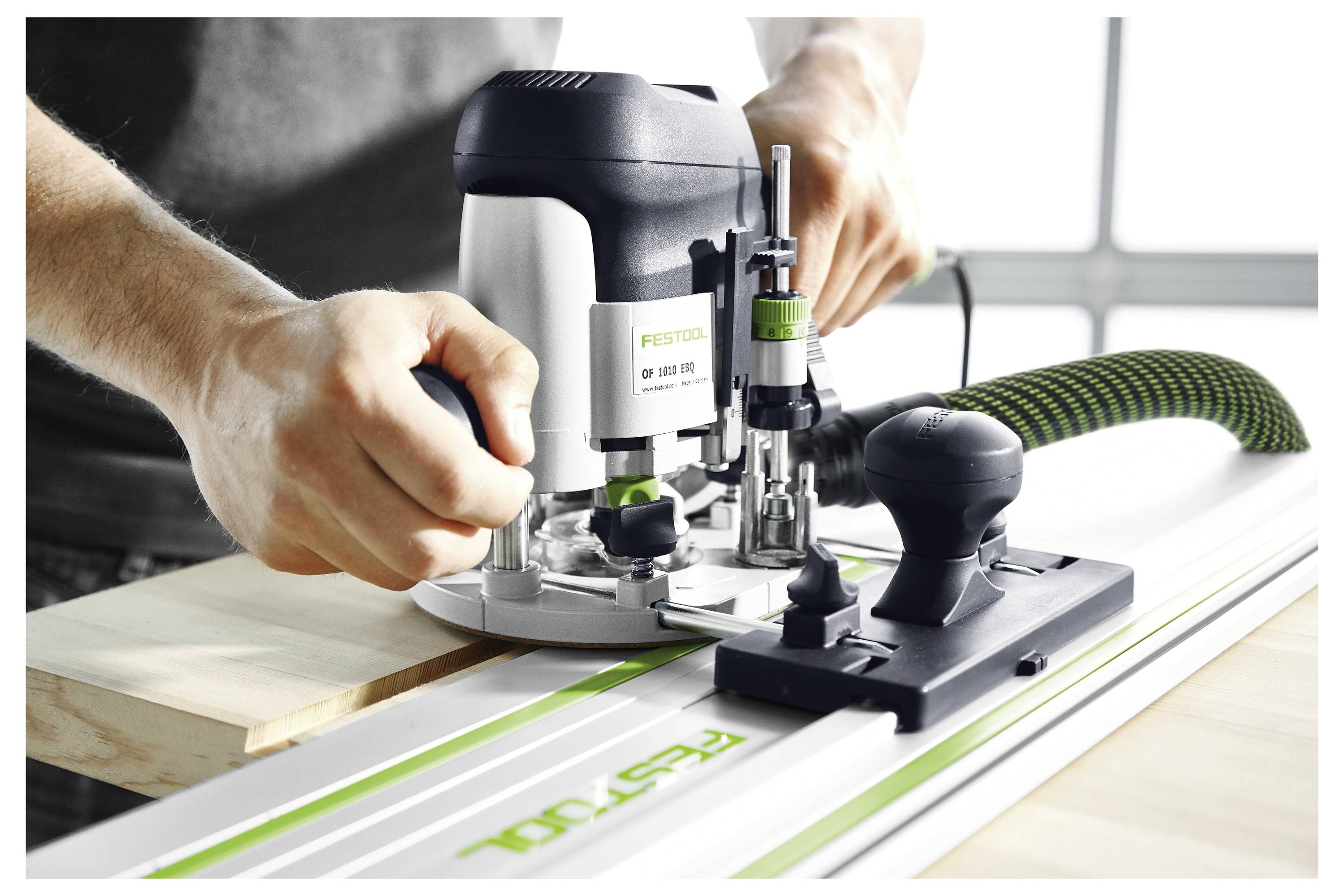 Een persoon bedient een Festool router op een geleiderailsysteem, wat demonstreert hoe nauwkeurig houtwerk wordt uitgevoerd met aandacht voor gereedschapshantering en uitlijning.