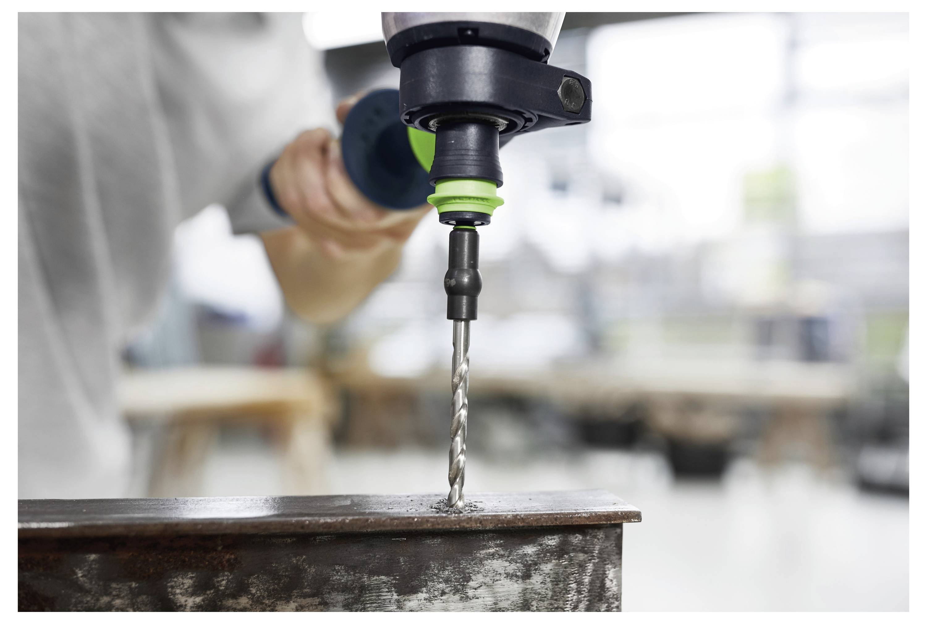 Een persoon die een accuboor gebruikt om een gat in een verroeste metalen balk in een werkplaatsomgeving te boren.