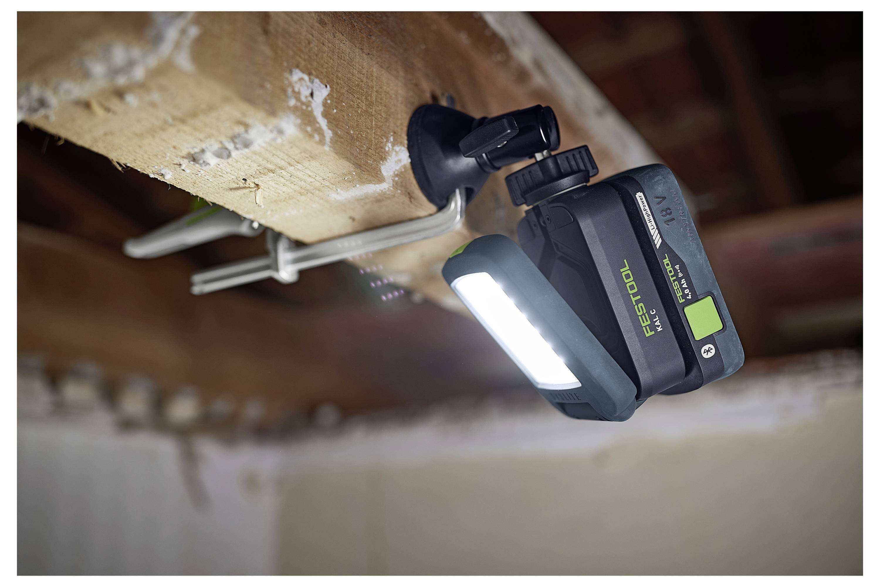 Een draagbare LED-werklamp bevestigd aan een houten balk, die een werkplek verlicht. Geschikt voor handen-vrij gebruik bij bouw- of reparatiewerkzaamheden.