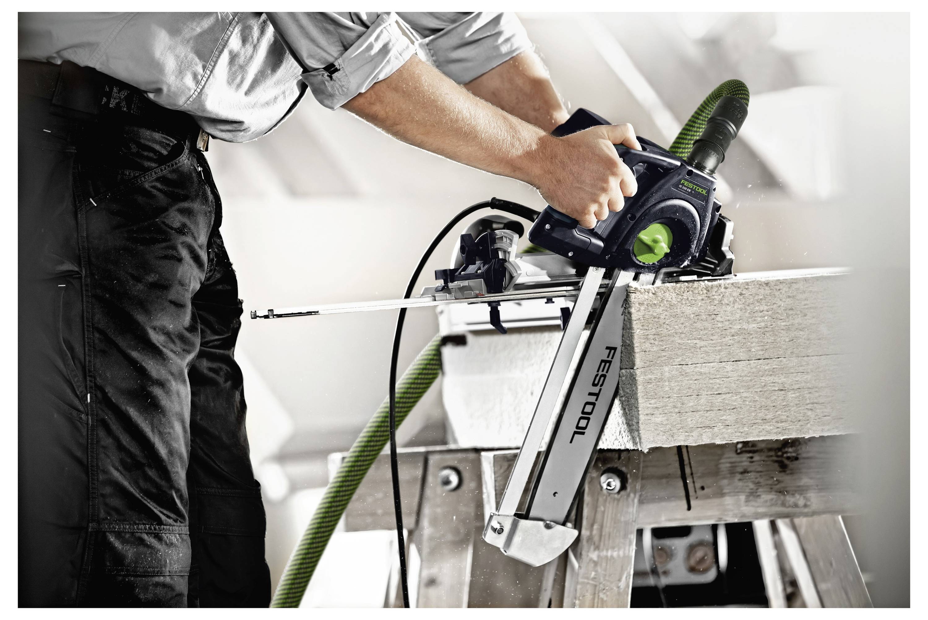 Een persoon gebruikt een Festool cirkelzaag om een houten plank, gepositioneerd op een zaaghuis, in een werkplaatsomgeving in te zagen.