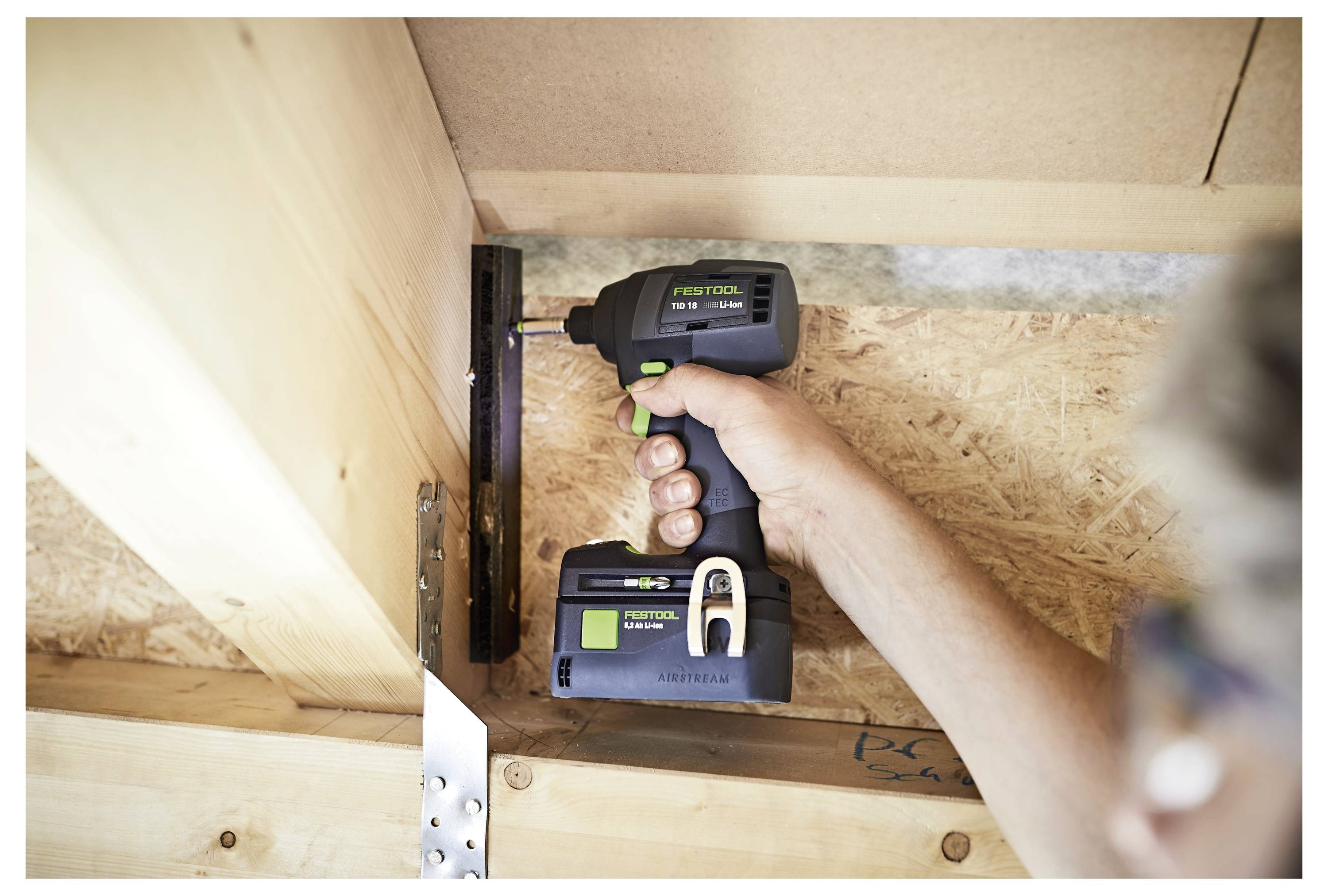 'Close-up van een persoon die een Festool-boor gebruikt om een houten balk in de bouw vast te zetten, met nadruk op precieze plaatsing en handhoudpositie.'