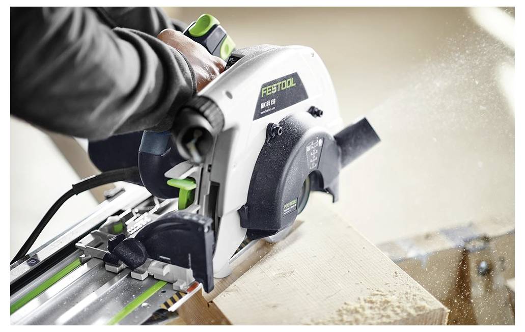 Een persoon gebruikt een Festool cirkelzaag om door een houten plank te zagen, waarbij zaagsel uit het zaagblad spat.