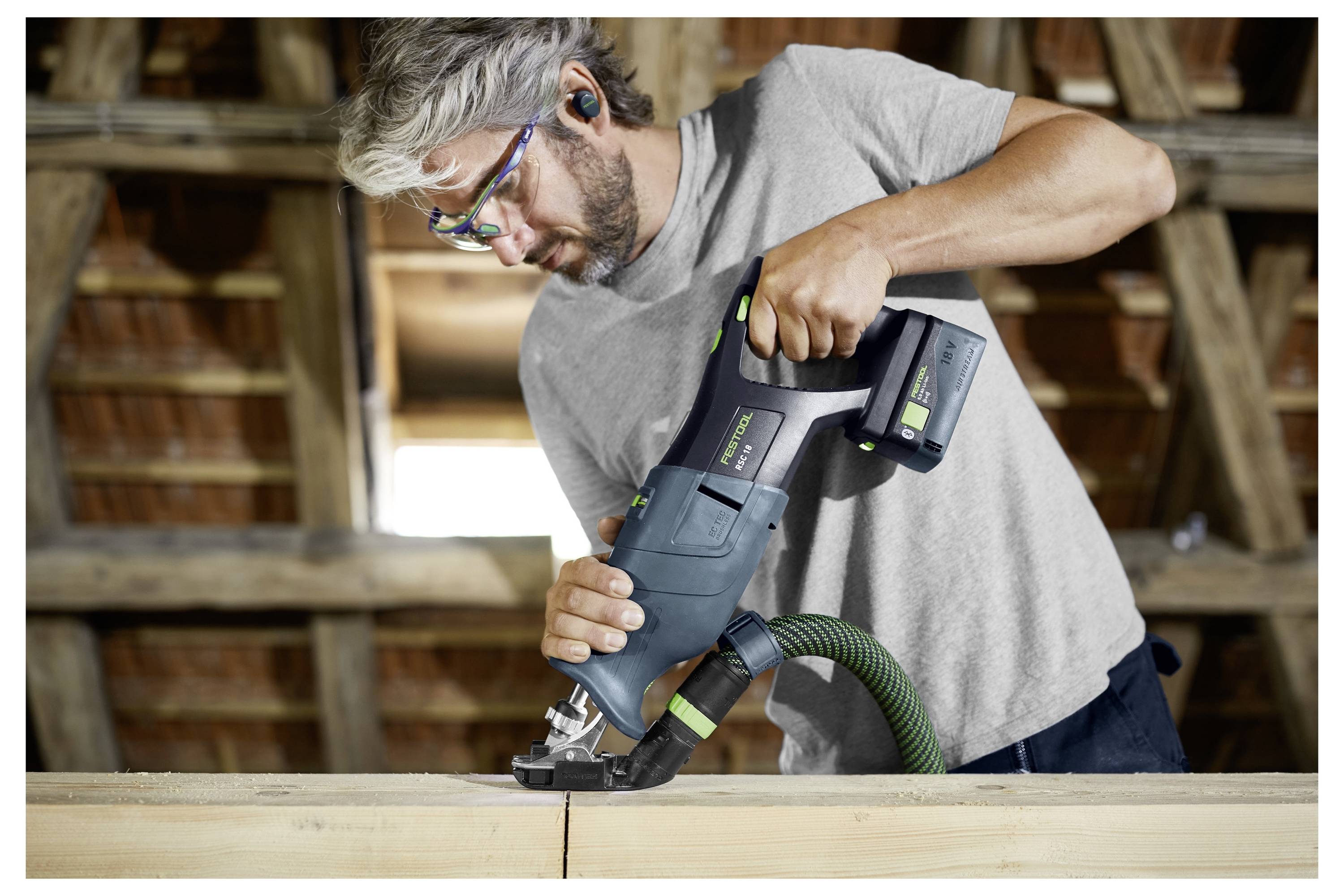 Een persoon die een elektische zaag gebruikt om een houten balk in een werkplaatsomgeving door te zagen.