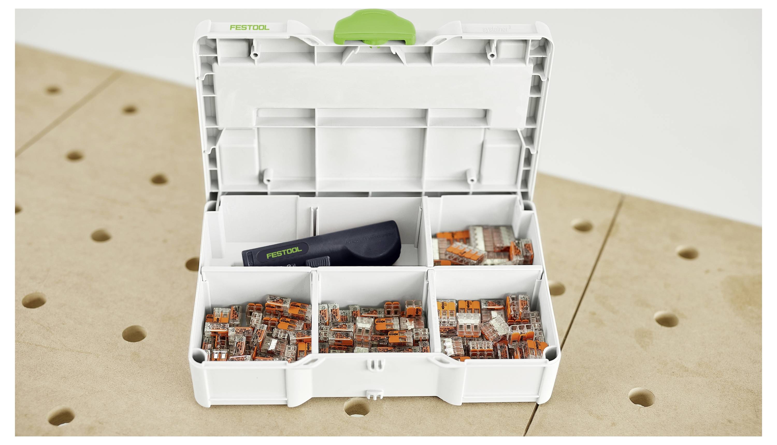 Een open Festool compartimentdoos gevuld met verschillende maten kabelconnectoren en een gereedschap op een houten oppervlak met gaten.
