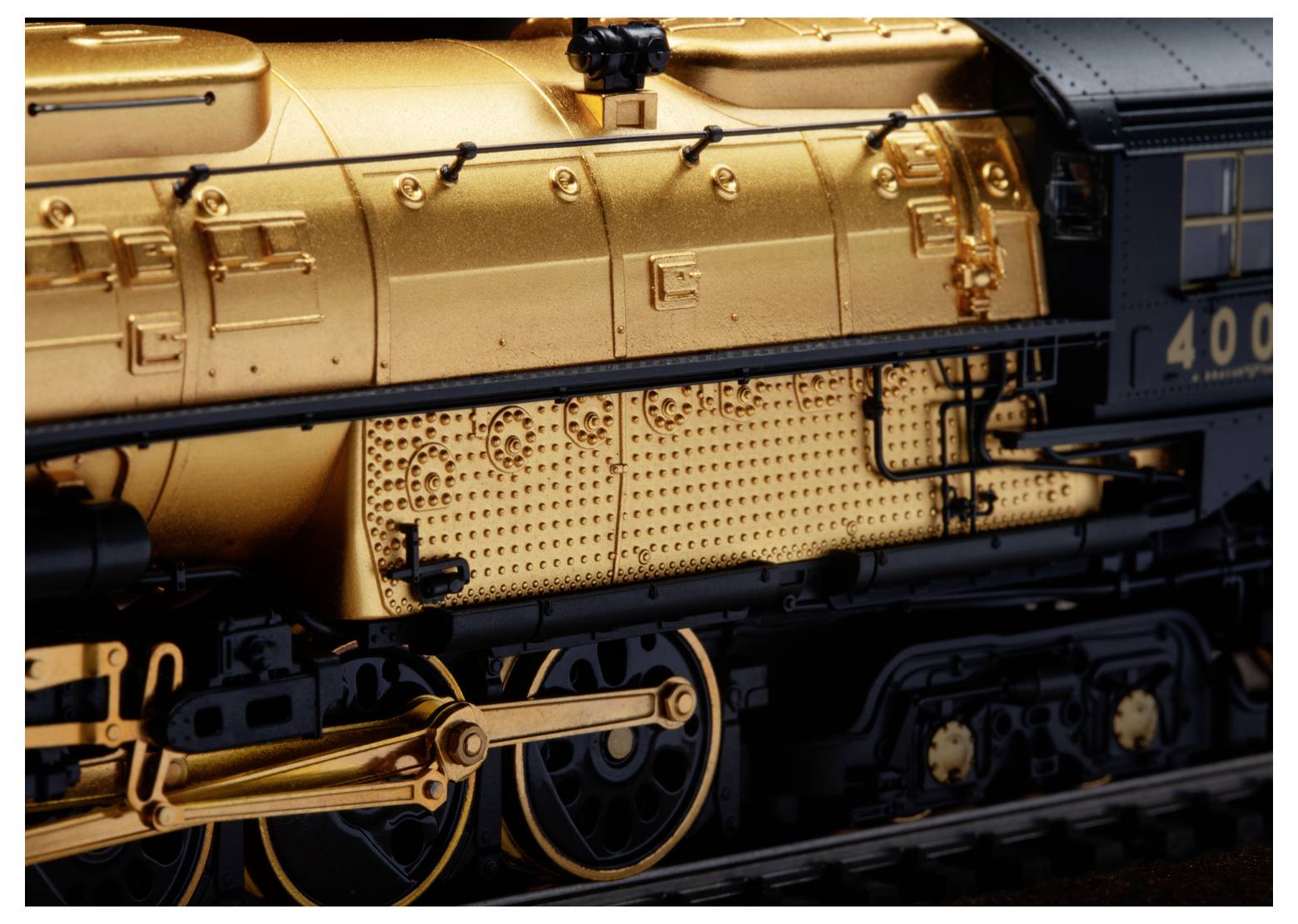 Close-up weergave van een modeltrain, met gedetailleerde goudgeschilderde machines en wielen, waarbij nadruk ligt op ingewikkelde ontwerpkenmerken.