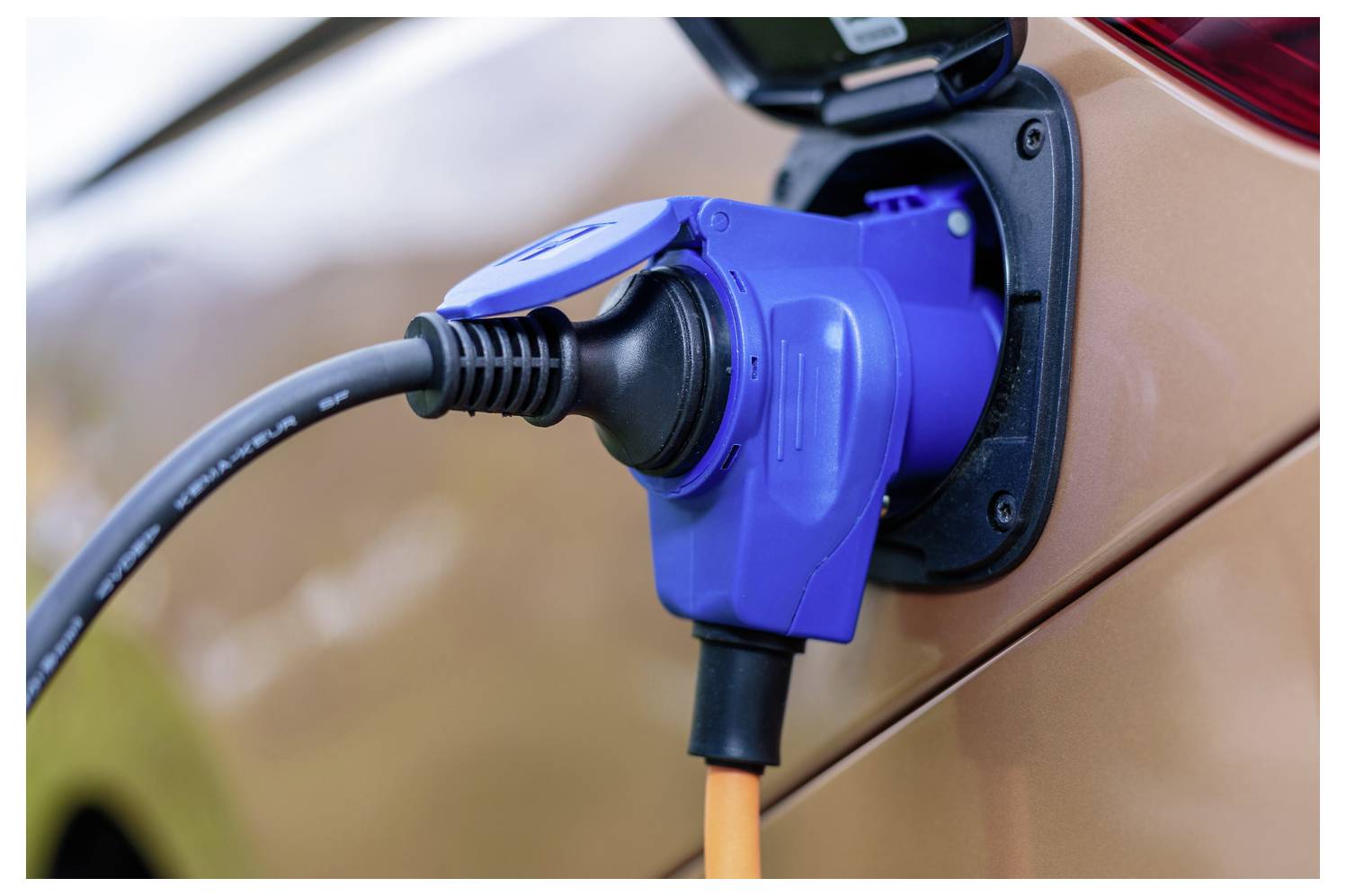 Close-up van een blauwe laadstekker voor elektrische voertuigen aangesloten op de laadpoort van een auto.