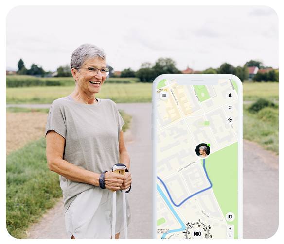 Een glimlachende persoon met kort grijs haar, gekleed in vrijetijdskleding, staat op een landelijk pad met wandelstokken. Een telefoon toont een kaart-app.