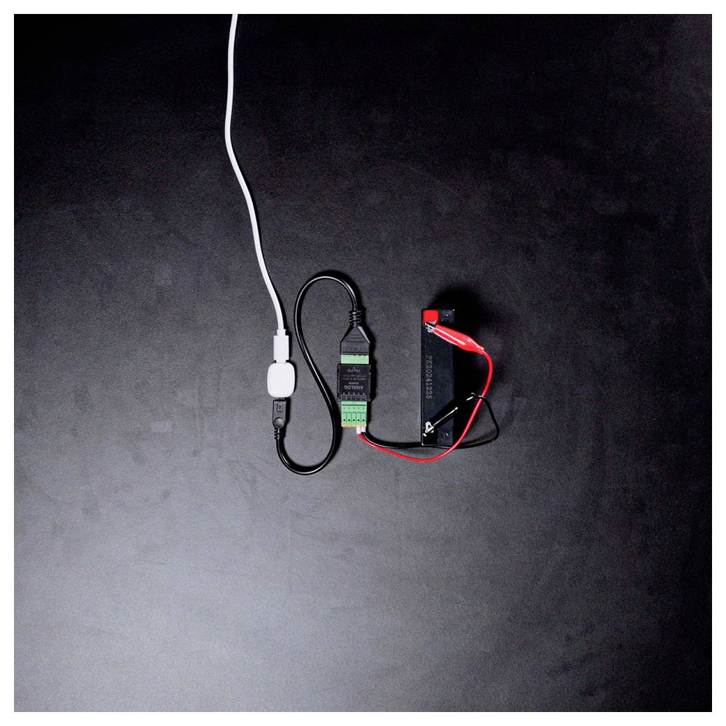 Een apparaat dat met draden op een donker oppervlak met een batterij is verbonden. De opstelling lijkt op een elektronicaproject of oplaadsysteem.